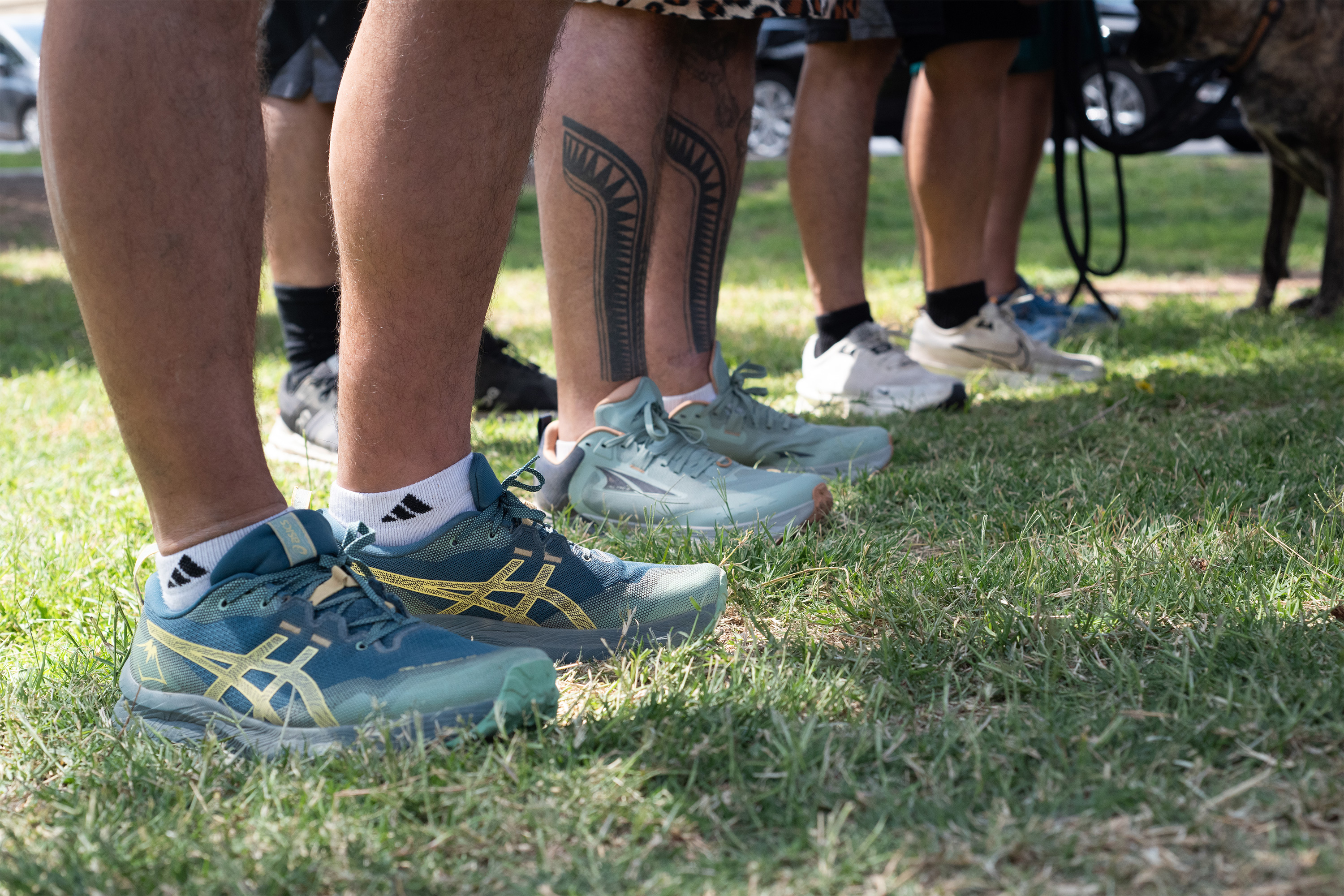 A close-up shot of runners' shoes as they stand on a patch of grass.
