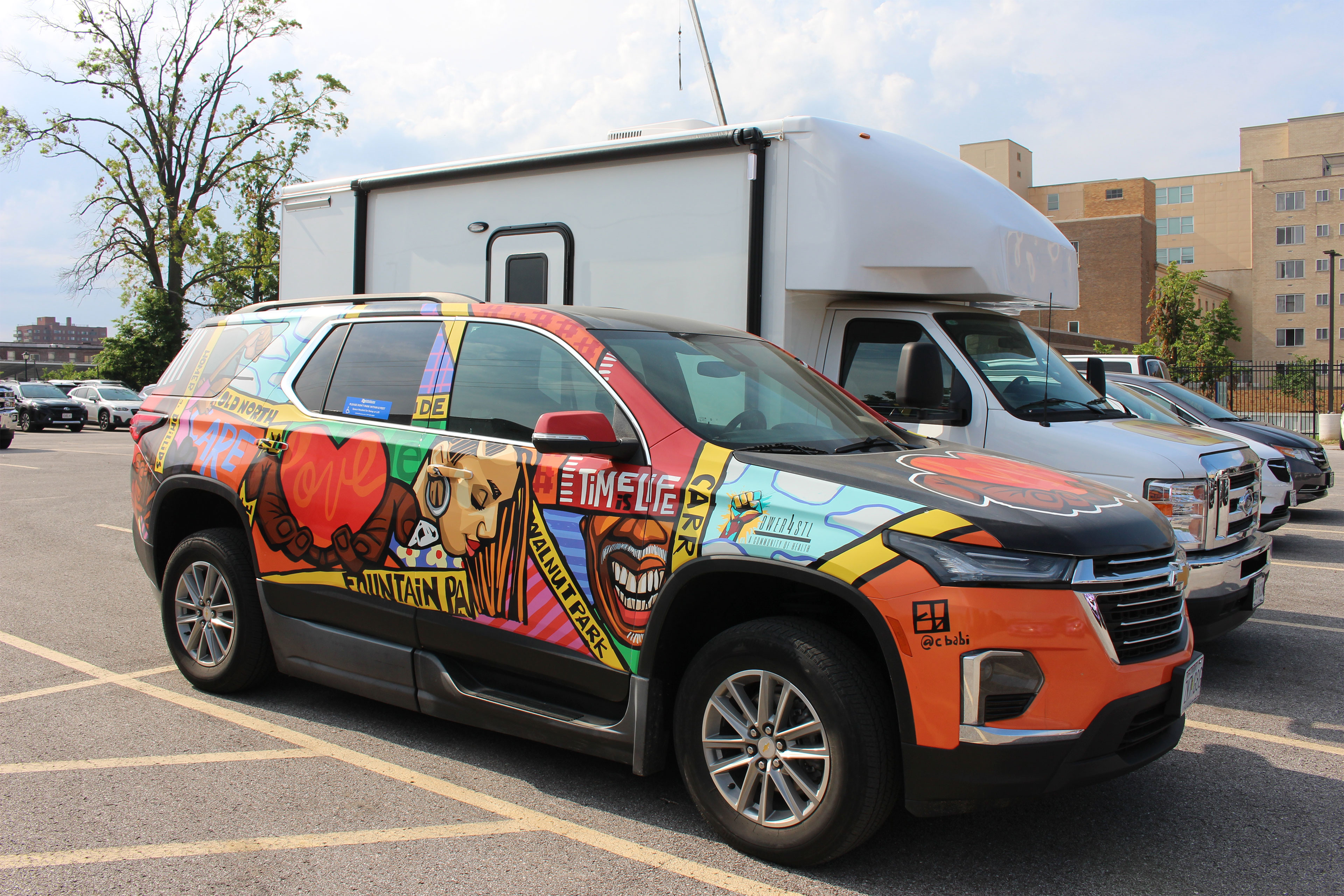 A colorfully decorated SUV is parked beside a white truck.
