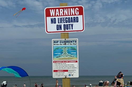 A photo of a warning sign on a beach that reads, "No lifeguard on duty."