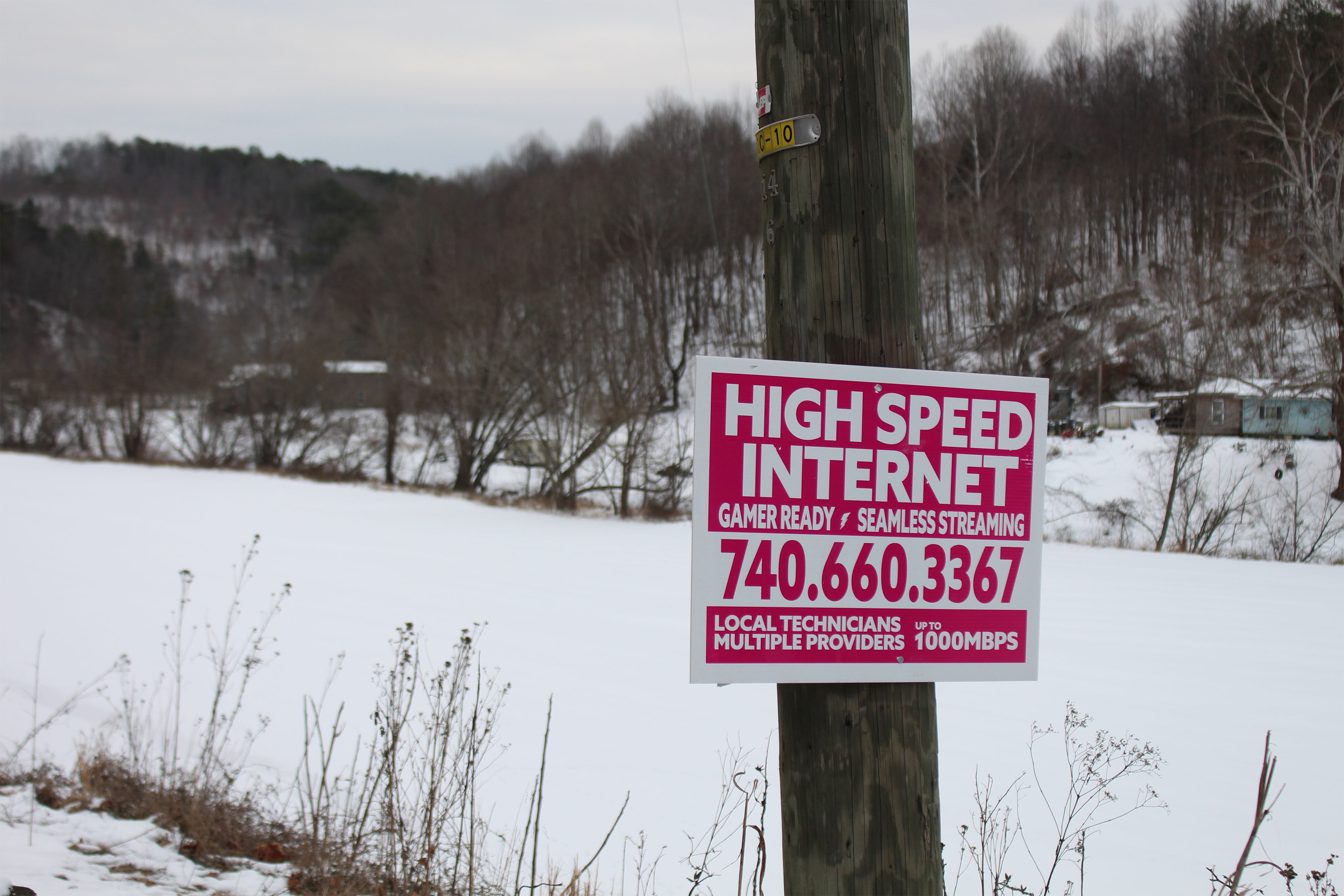 A sign attached to a wooden pole reads "High Speed Internet, Gamer Ready, Seamless Streaming, 740-660-3367, Local Technicians, Multiple providers, Up to 1000Mbps."