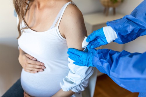 A photo of a pregnant woman sitting in a clinic, receiving a covid-19 vaccine.