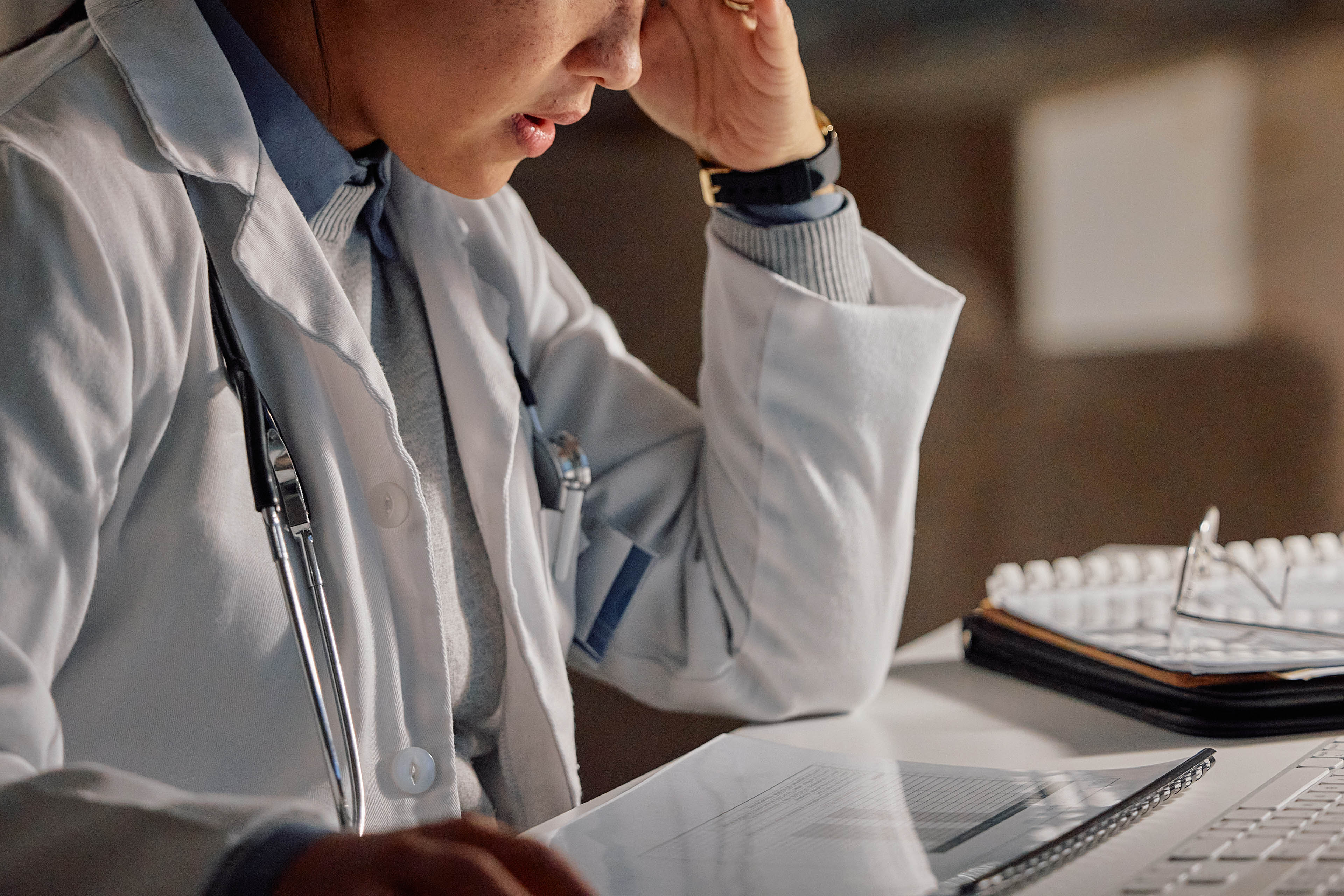 An unidentifiable female doctor works at a desk deep in thought.