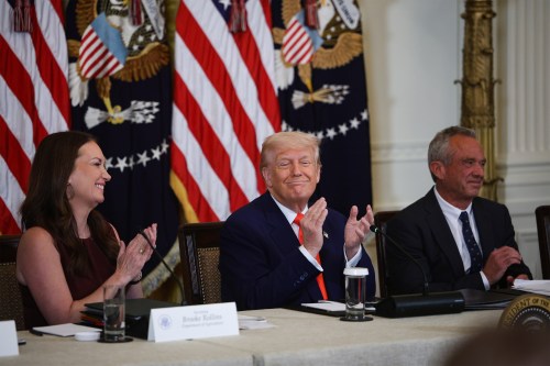 A photo of a White House event with three people sitting at the end of the table: Brooke Rollins, Donald Trump, and Robert F. Kennedy Jr.