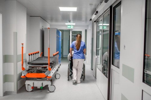 A photo of a nurse pushing a patient in a wheelchair in a hospital corridor.