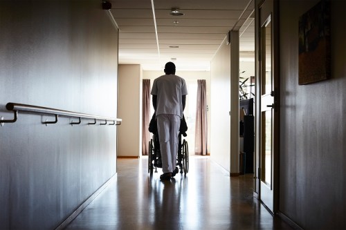 A photo of a nurse wheeling his patient in a wheelchair in a nursing home.