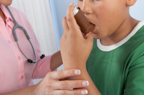 A photo of a nurse helping a young boy use an asthma inhaler.