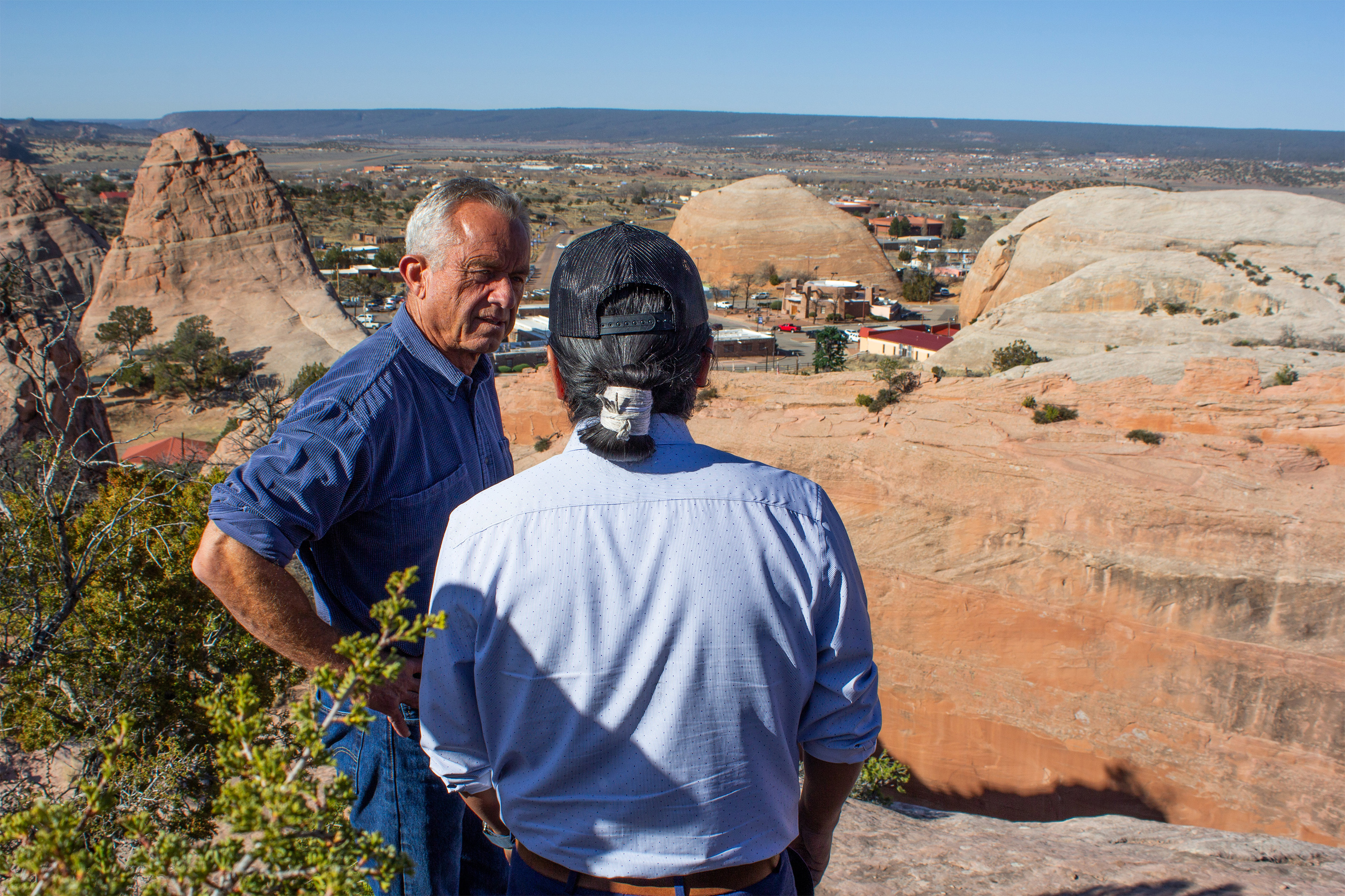 A photo of Robert F. Kennedy listening as Buu Nygren (seen from behind) speaks to him. A rocky landscape is seen behind them.