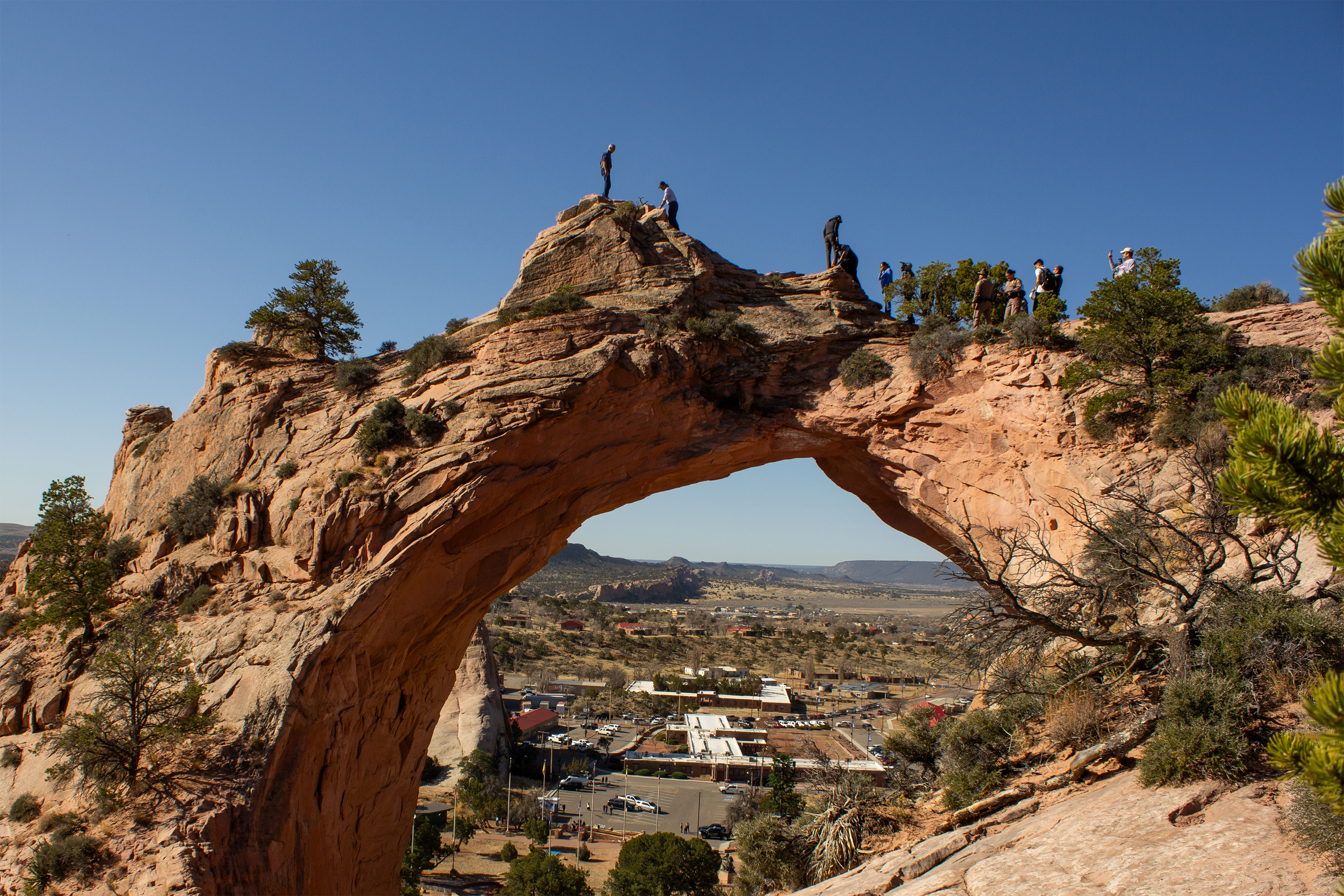 A photo of a large bridge-shaped sandstone formation arcing across a desert landscape.