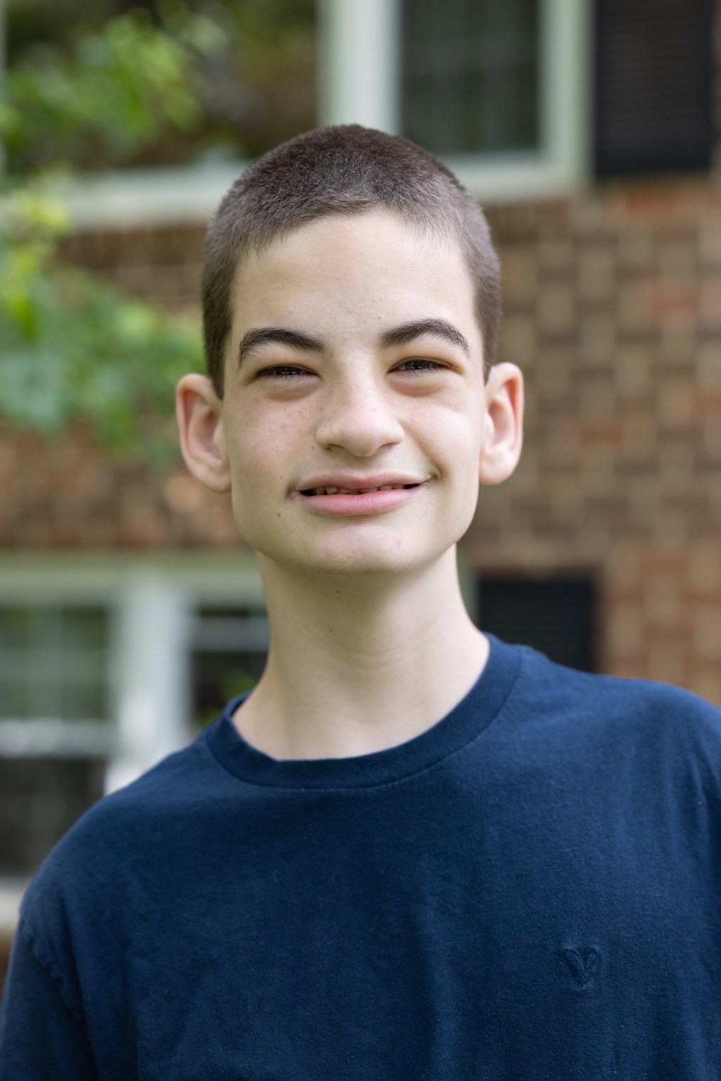 A young man wearing a navy t-shirt and with a shaved head, smiles at the camera.