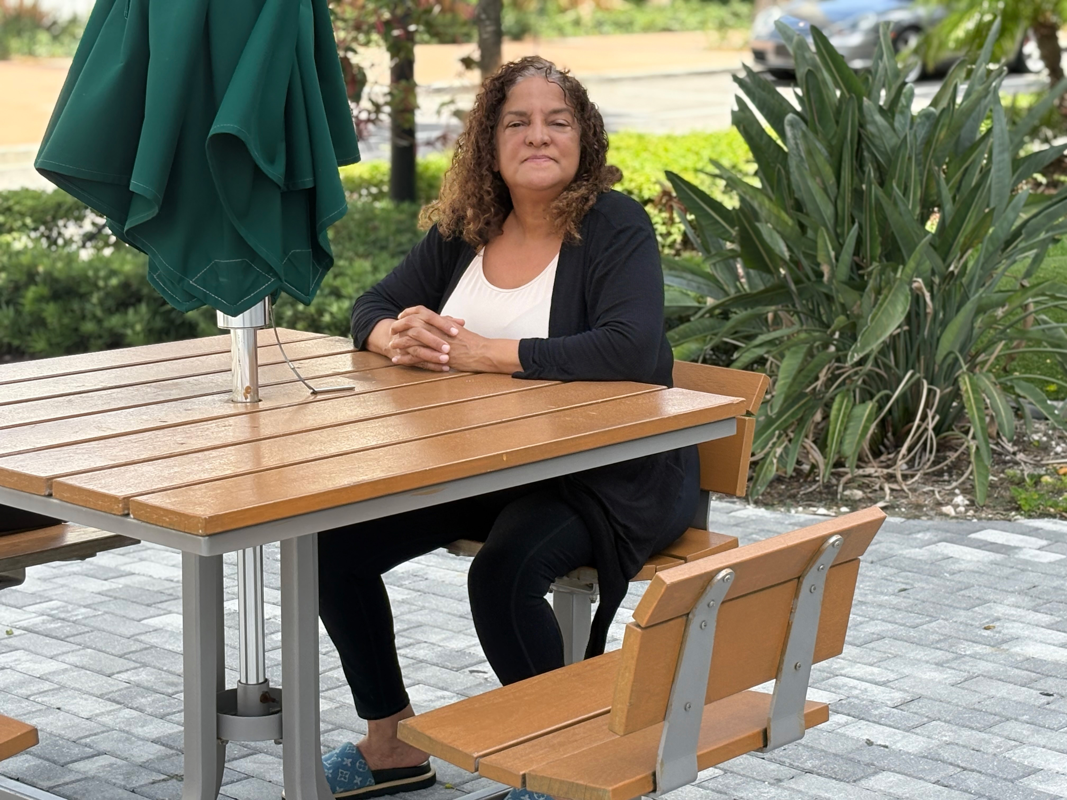 A photo of a woman sitting at a table outside.