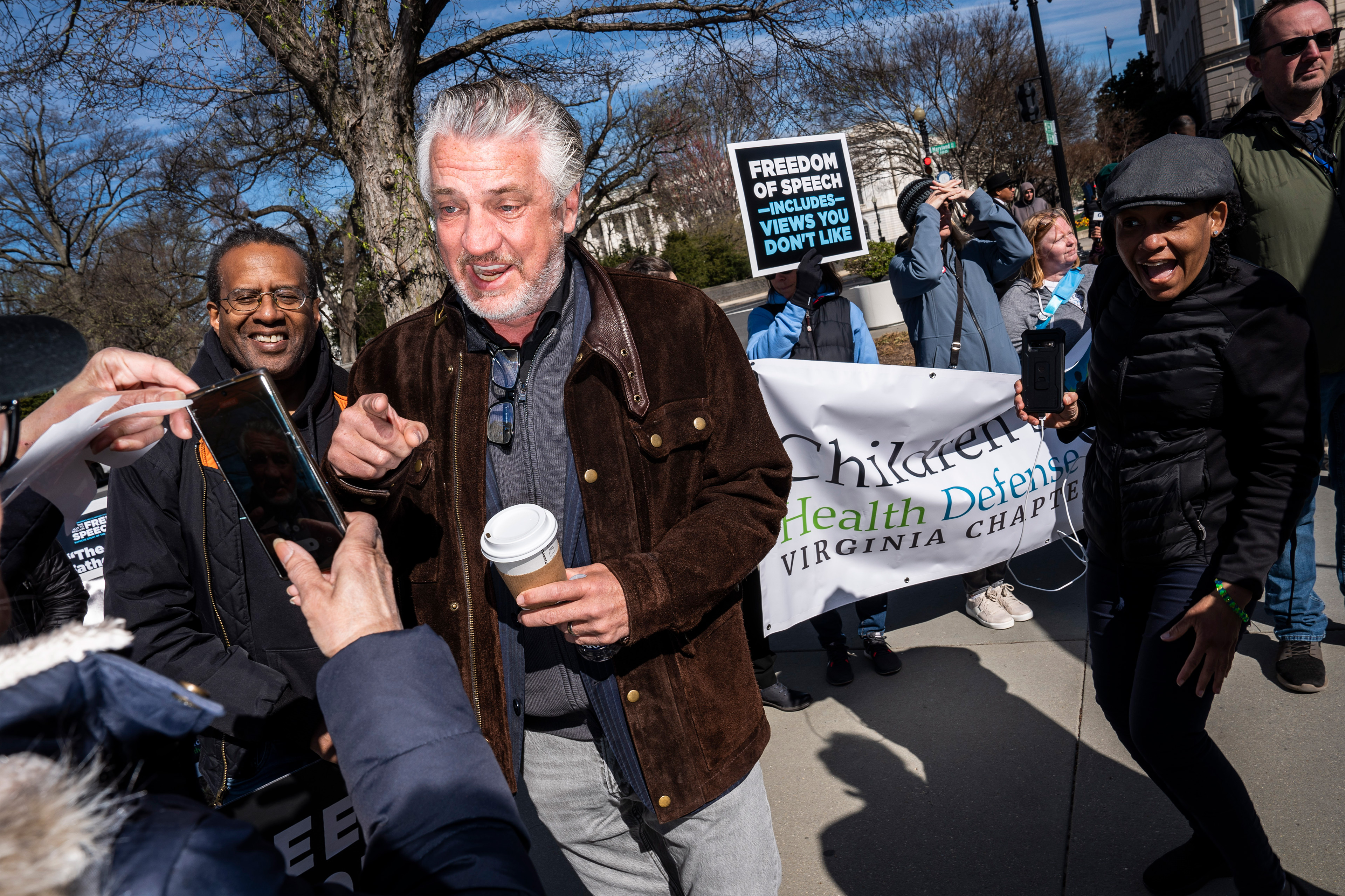 A photo of Del Bigtree speaking to people at a rally. A large banner with Children's Health Defense's logo is seen behind him.