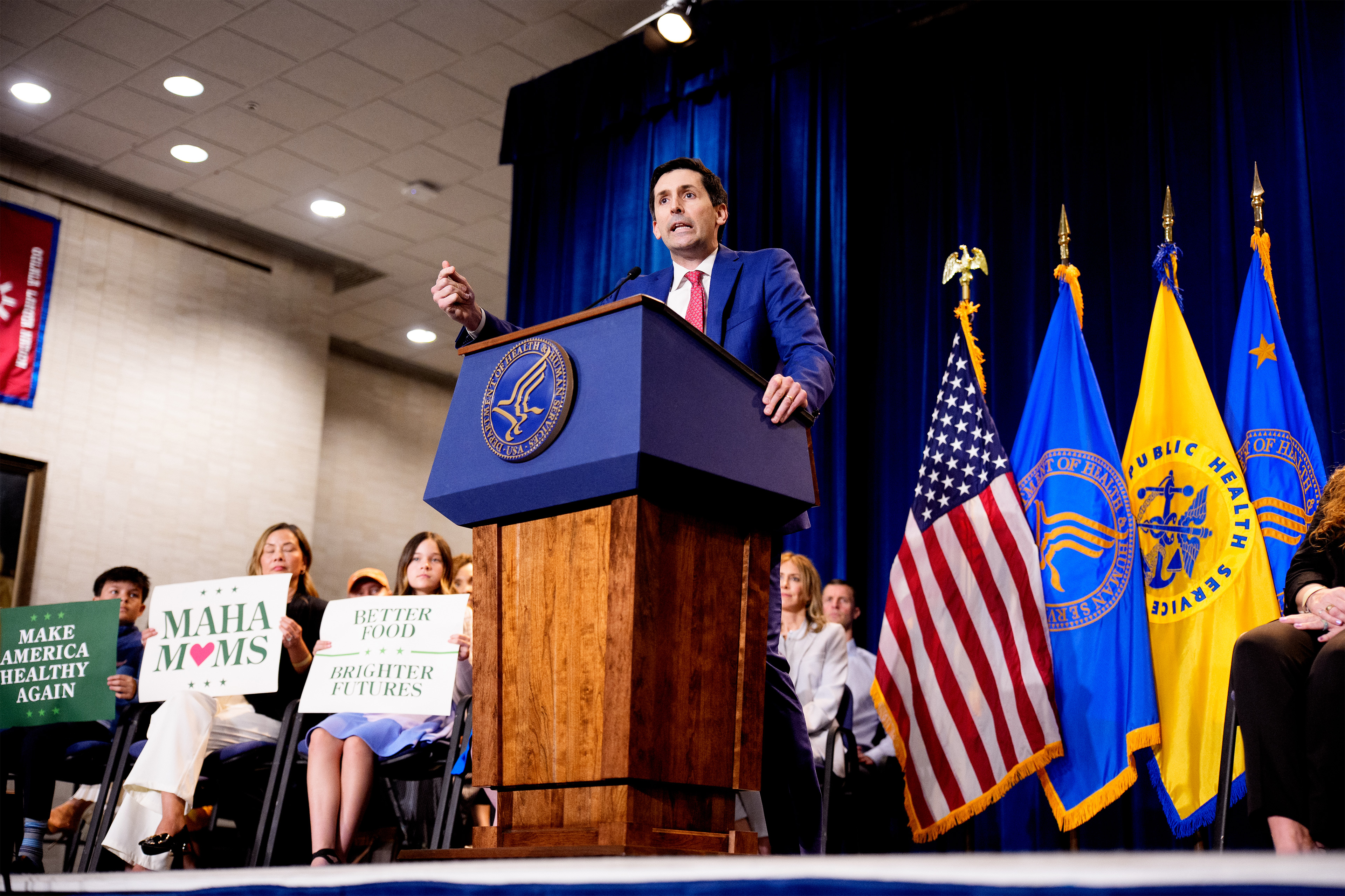 A photo of Calley Means speaking at an event at the Department of Health and Human Services behind a podium.