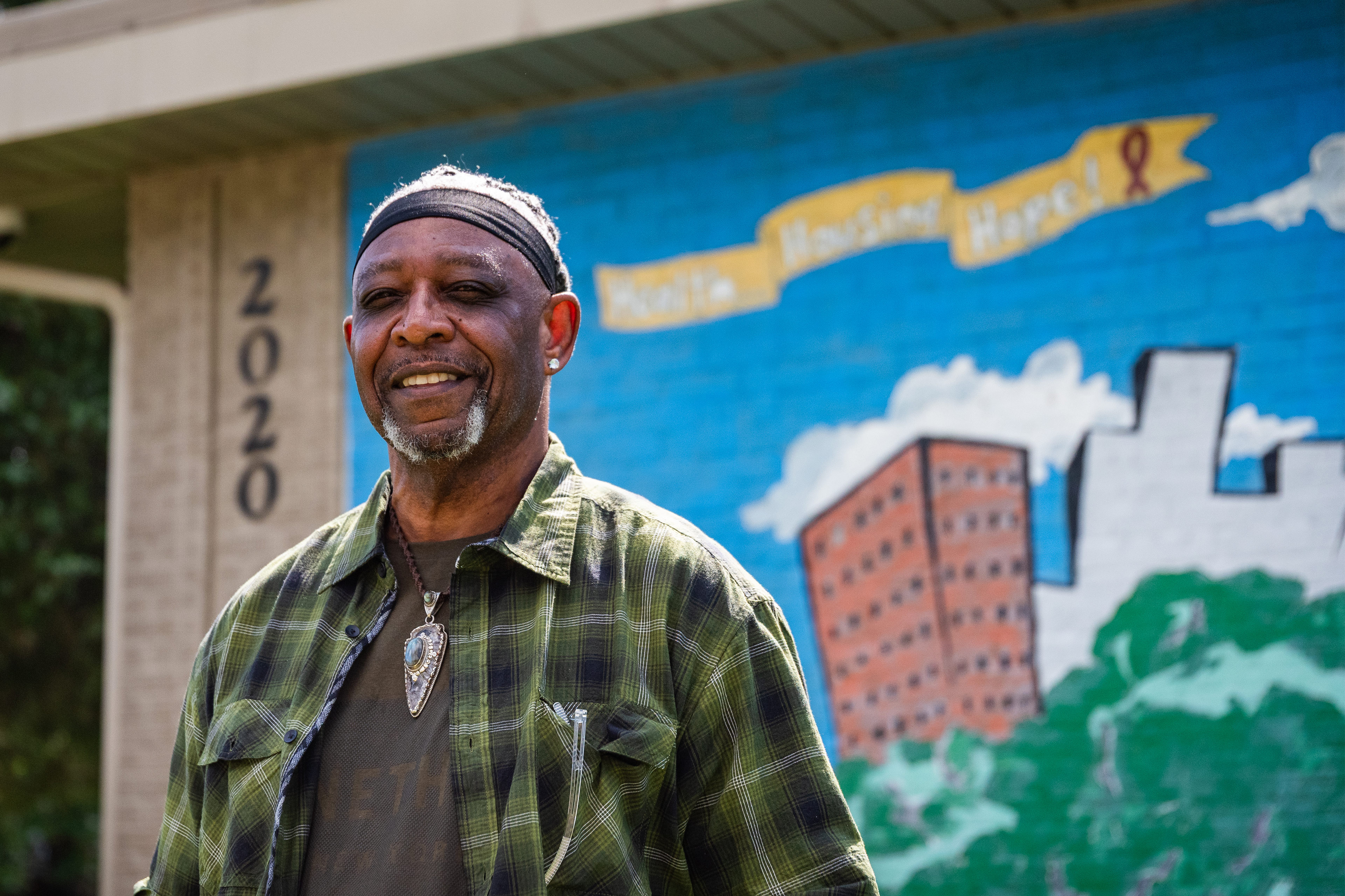 A portrait of Robert Smith smiling outside. A mural of the city is behind him.