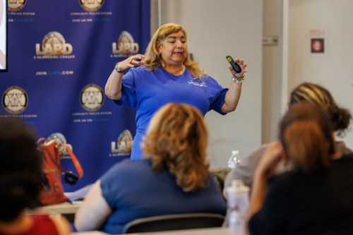 A woman wearing a blue shirt stands in front of a group of people as she gives a presentation