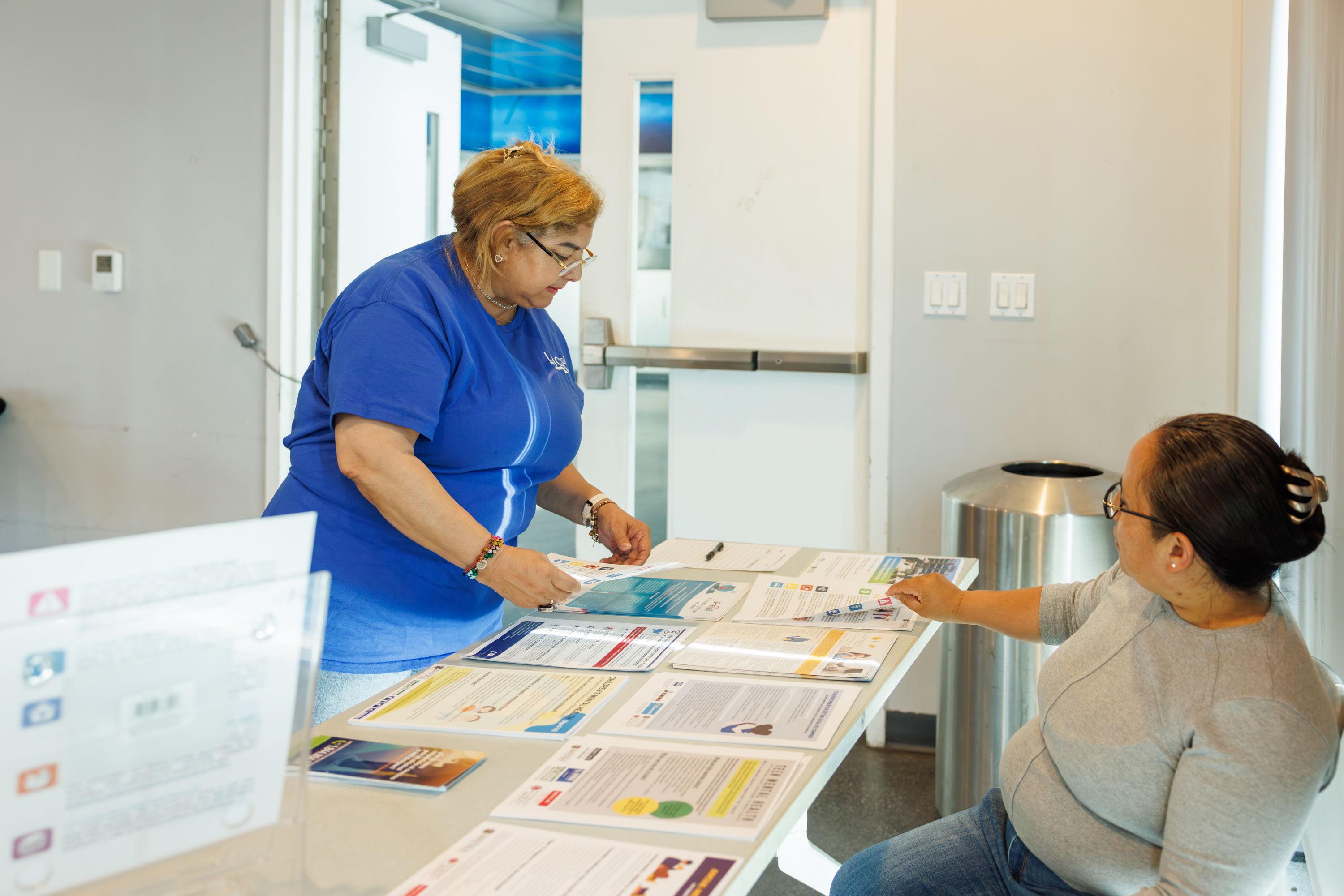 A woman wearing glasses and a blue t-shirt stands as she organizes flyers on a table