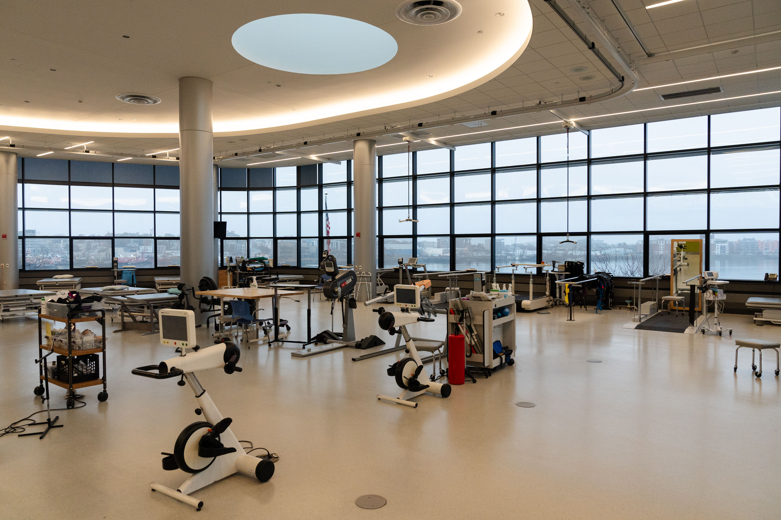 Exercise machines sit in a bright room with many windows and high ceilings