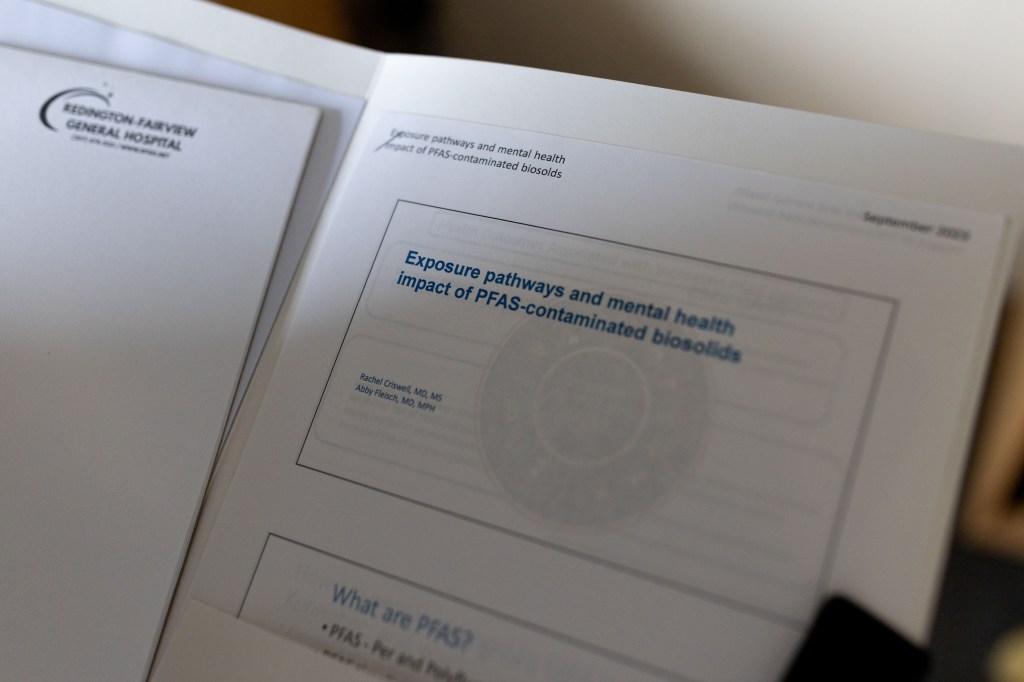 A close up shot of some research papers in a folder. The top paper reads: "Exposure pathways and mental health impact of PFAS-contaminated biosolids."