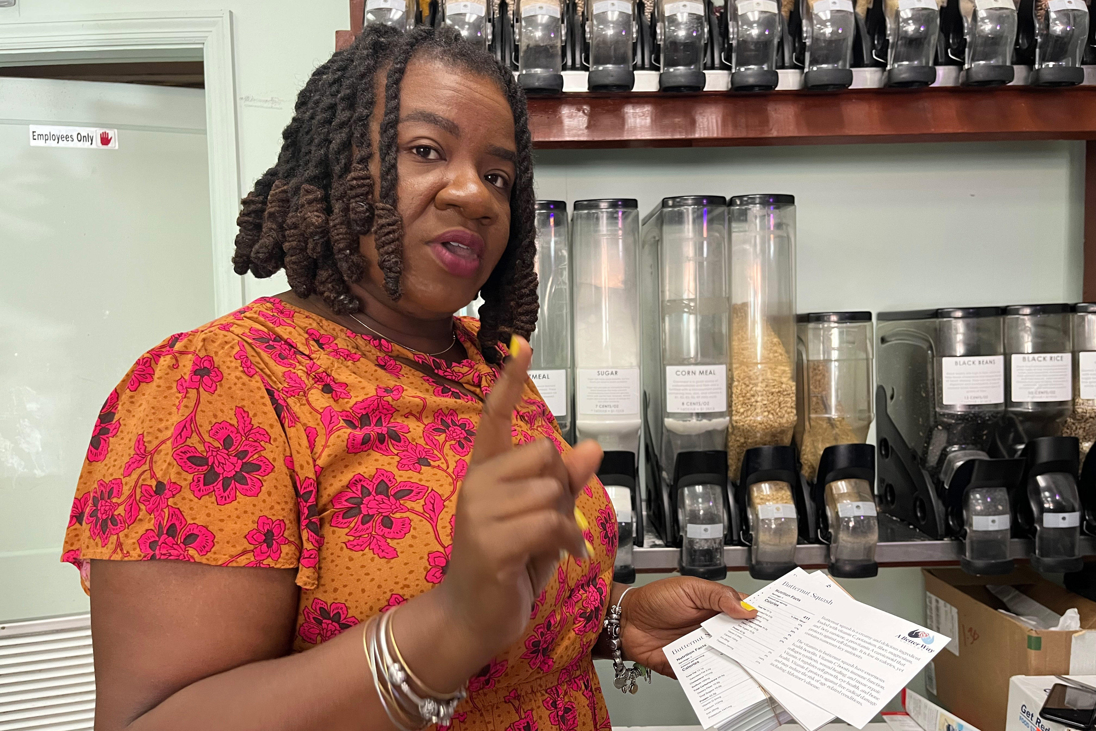 A photo of Terrell posing by a series of dispenser in her grocery store for dry goods such as beans, corn meal, and sugar.
