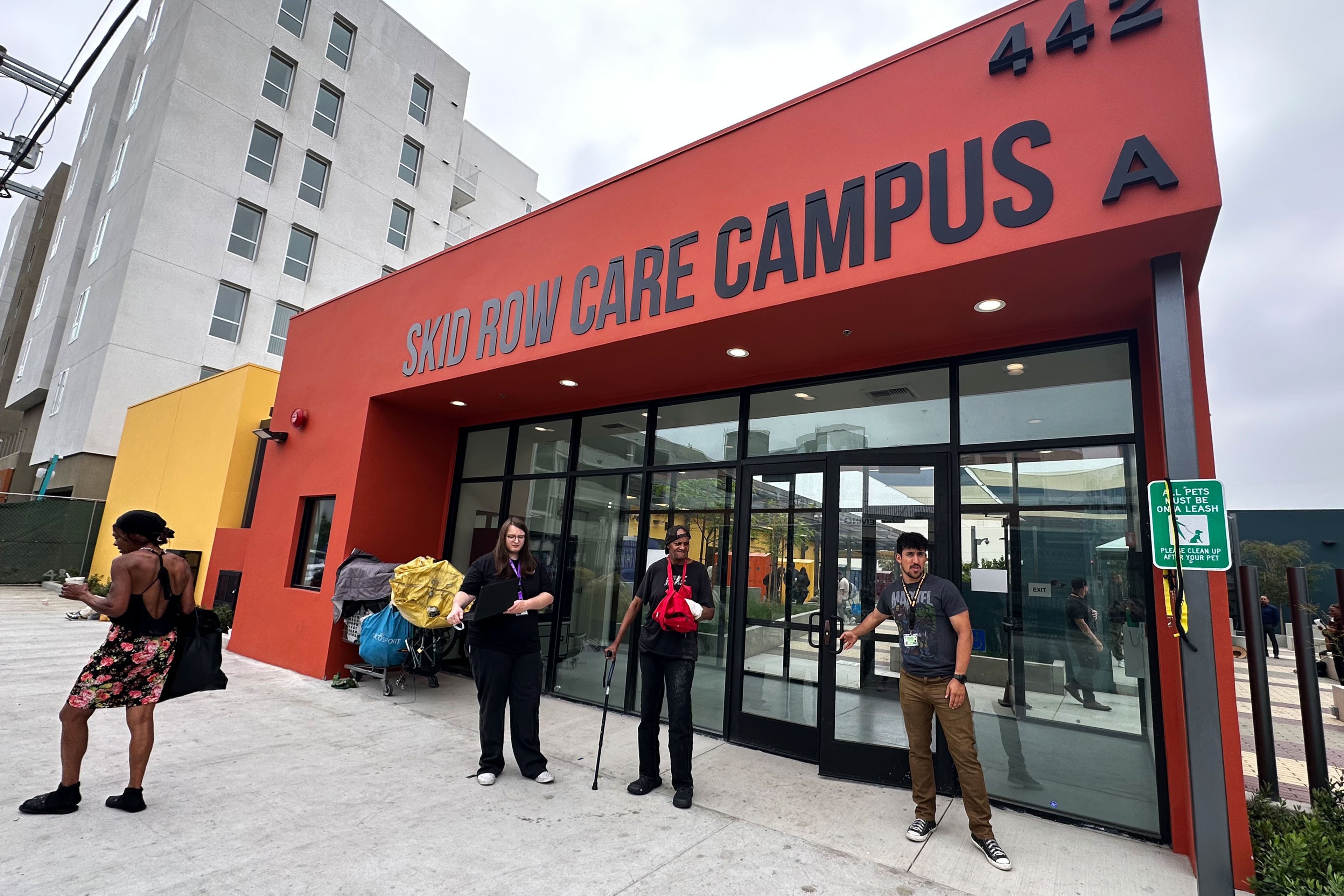 An exterior photograph of a building with large glass doors. The sineage above reads, "SKID ROW CARE CAMPUS."