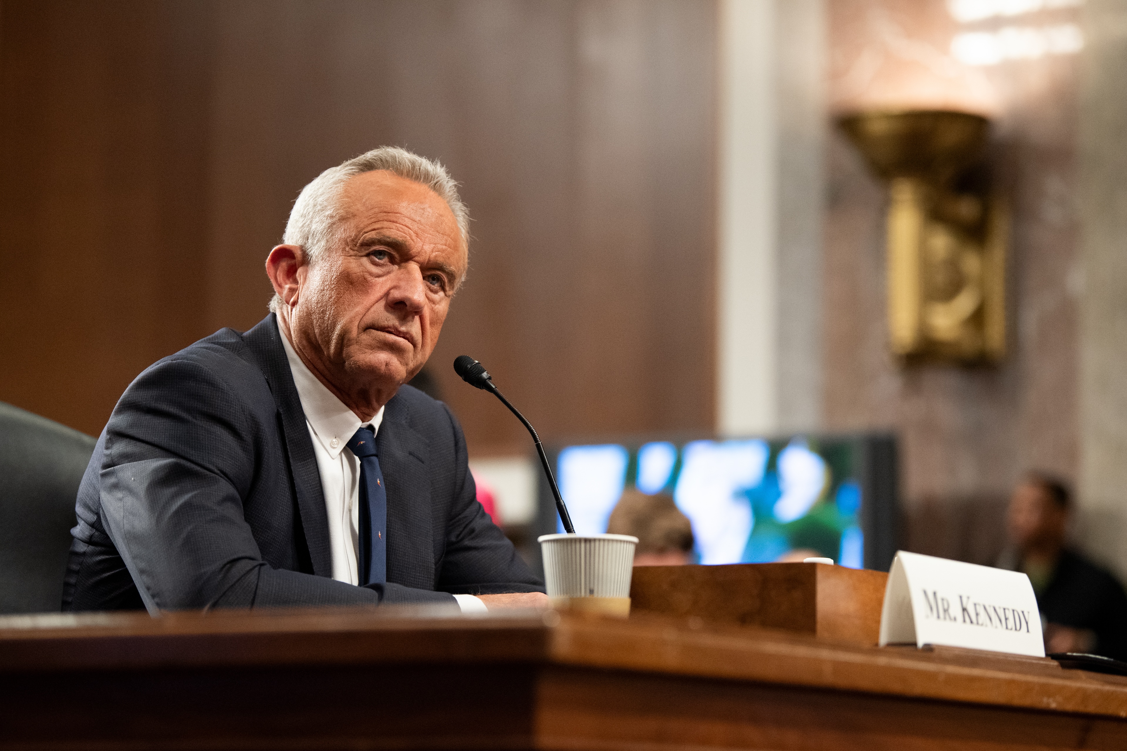 A man in a suit, Robert F. Kennedy Jr., with gray hair is seated at a desk before a microphone.
