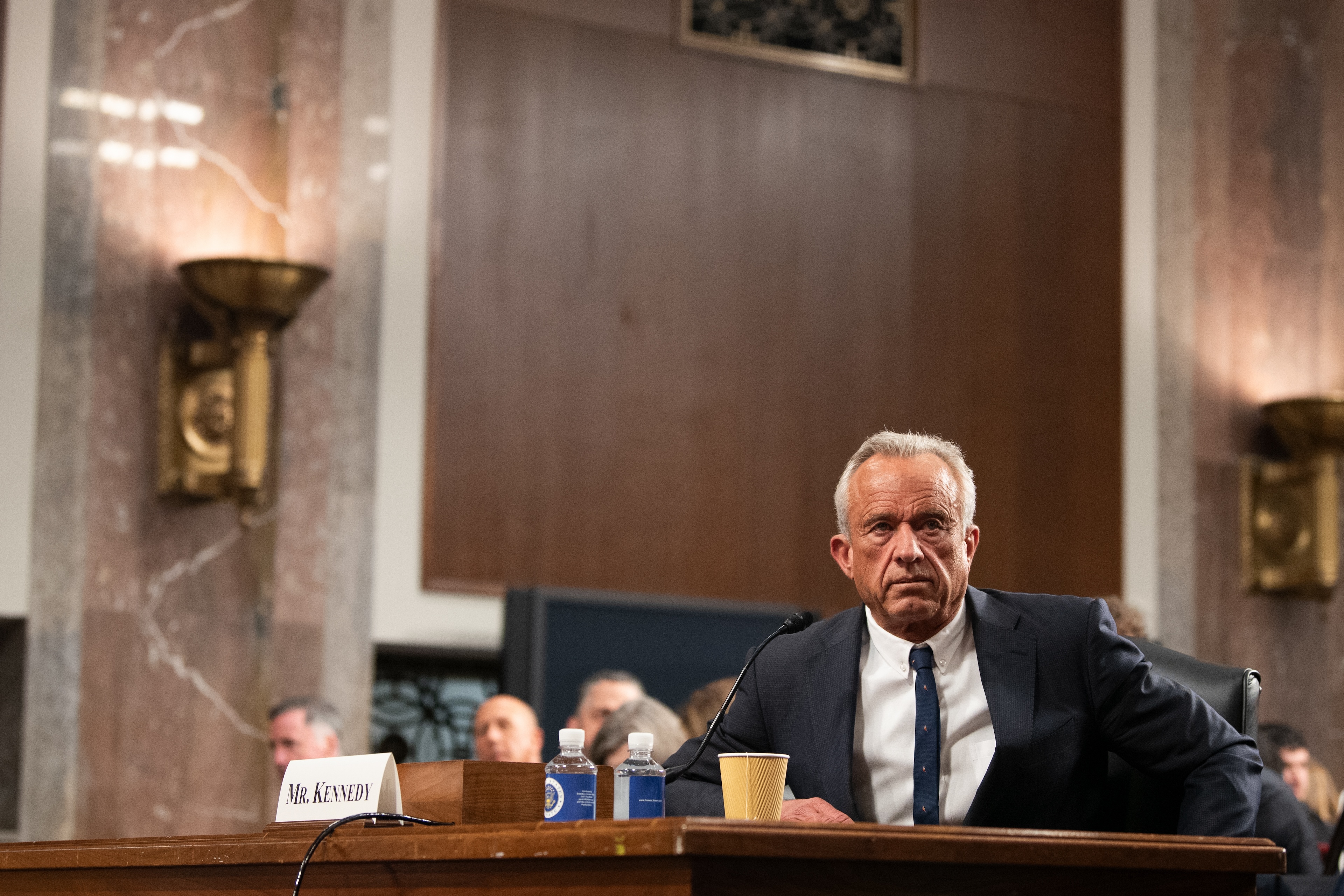 Robert F. Kennedy Jr. dressed in a suit and tie seated at a table before a placard with his name on it