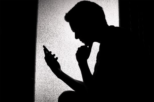 A photo of a young man in silhouette. He is looking at his phone.
