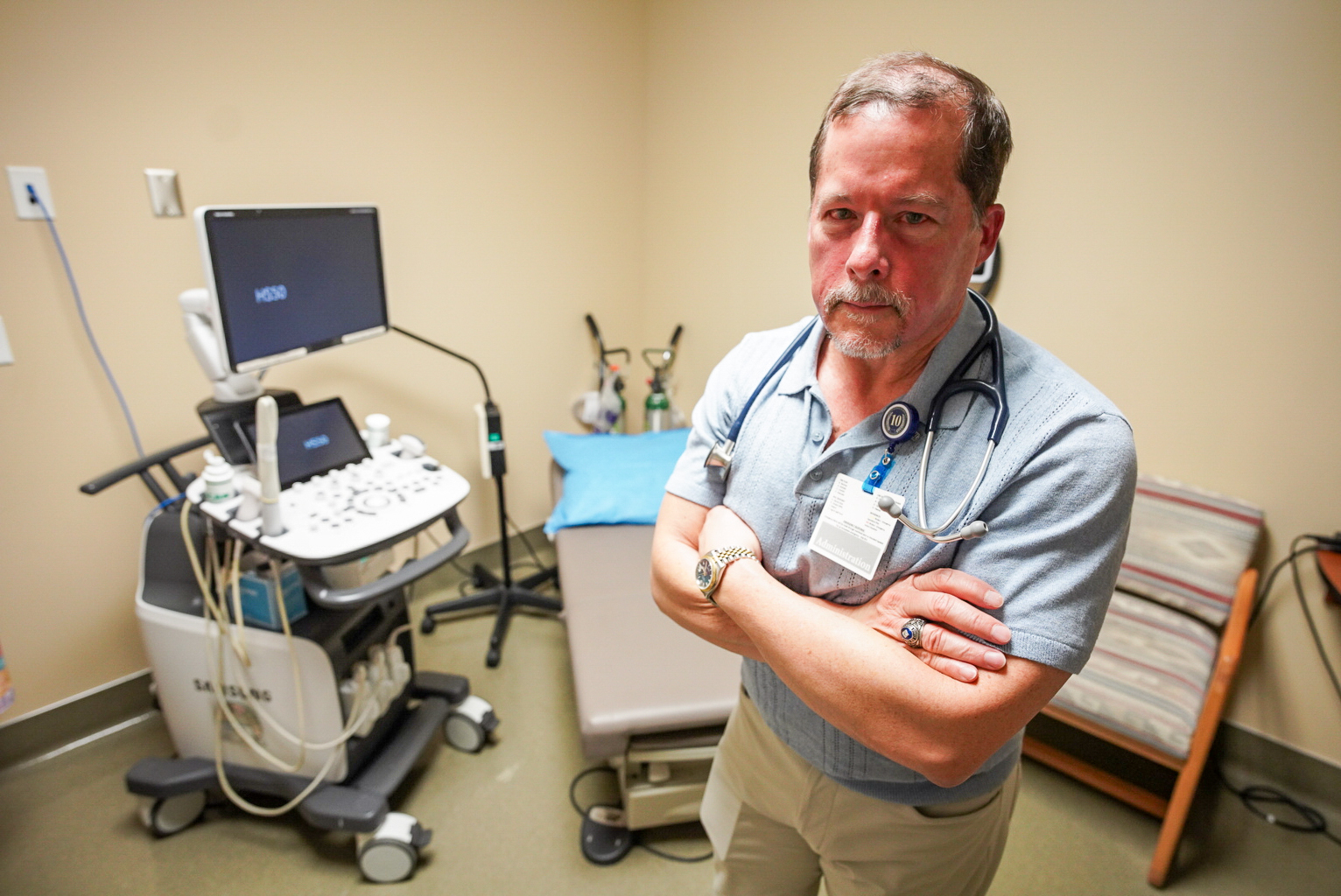 A photo of a male doctor standing with his arms crossed in a medical room.