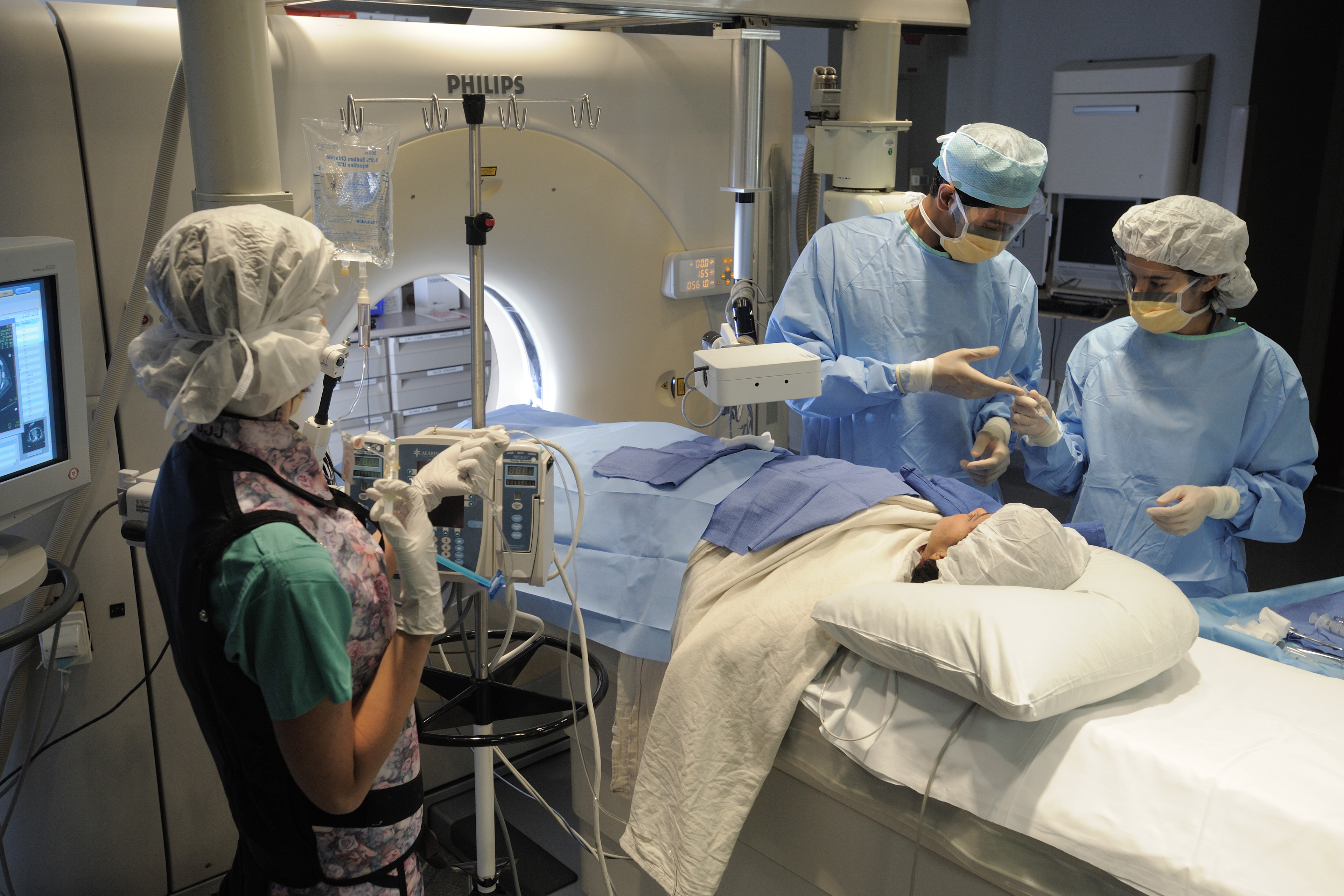 A photo of three medical workers in surgical garb treating a patient in front of an MRI machine.