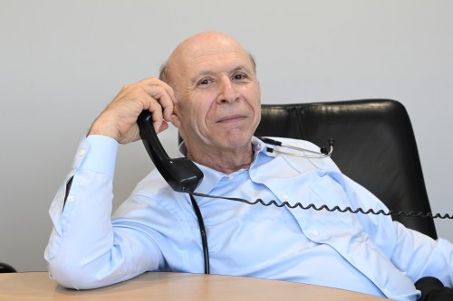 A photo of a doctor in his office, posing by holding a corded phone to his ear.