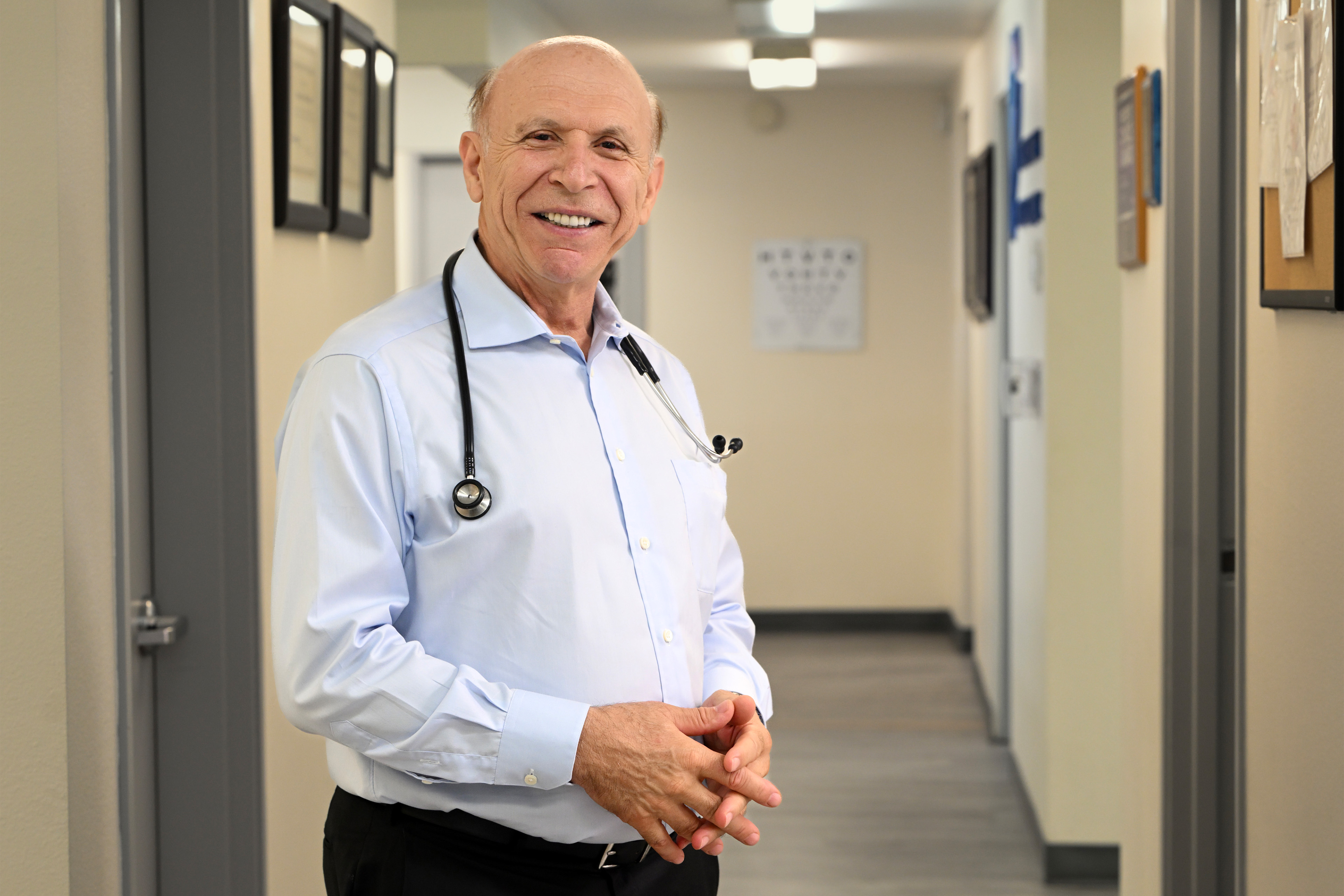 A photo of a doctor posing in his office with a stethoscope draped around his neck.