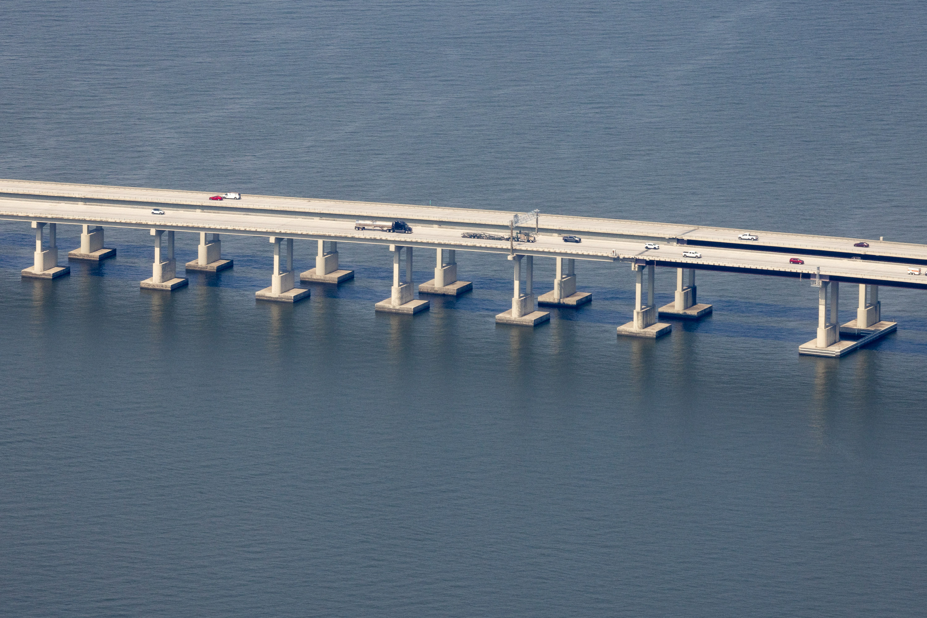 A view of a long bridge over a lake with shoulders on both sides of the bridge.
