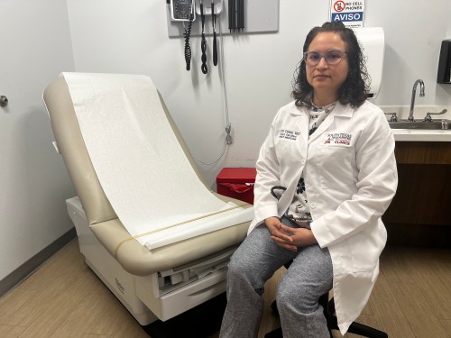 A photo of a doctor sitting by an exam chair in her office.
