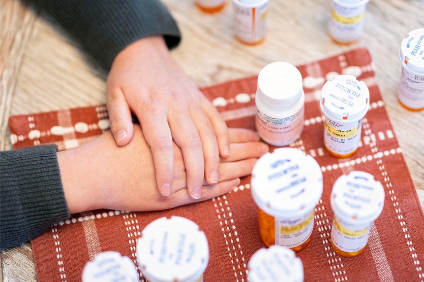 Sheldon Ekirch with her hands folded on a table next to her pill bottles.