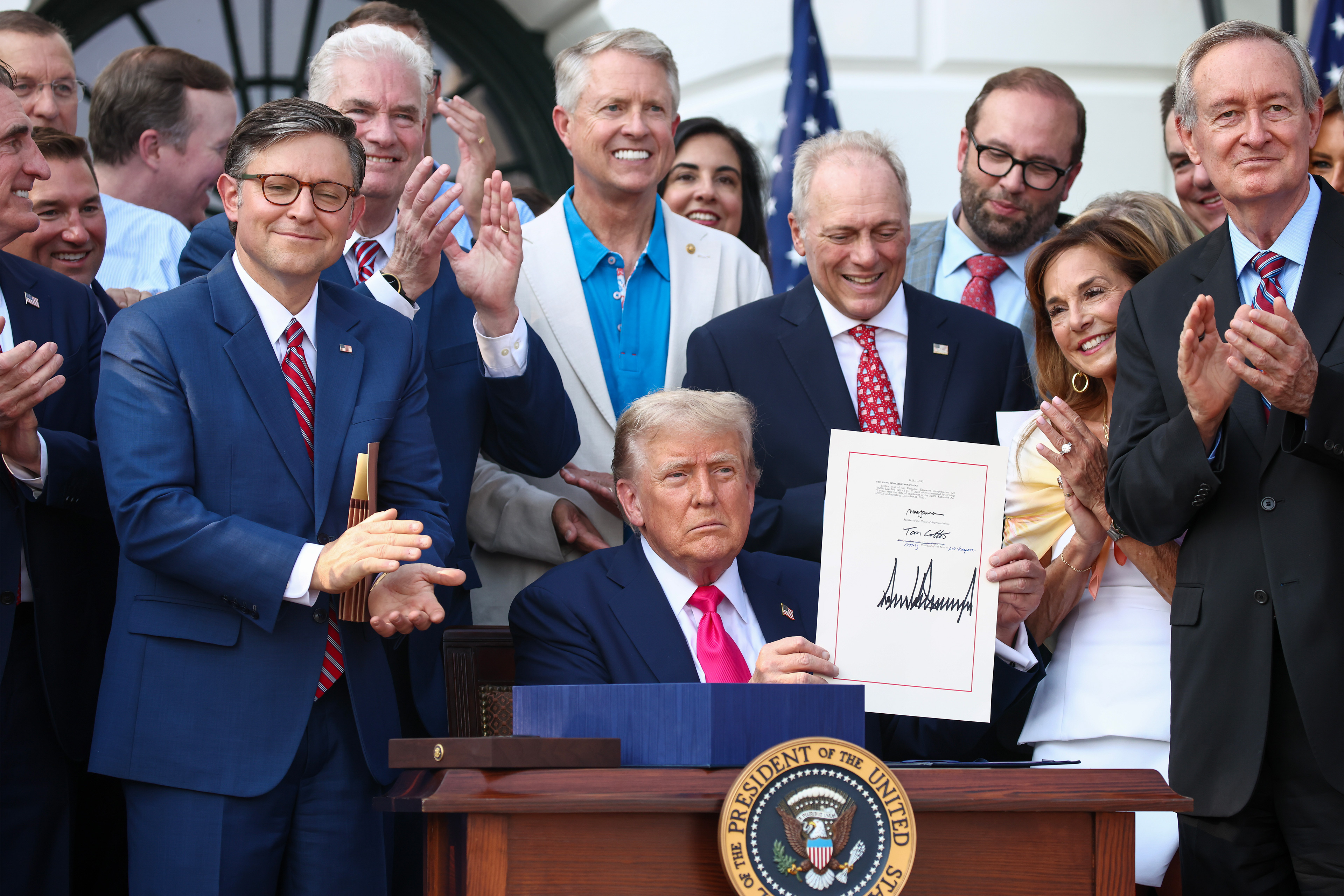 A photo of President Trump holding up his signed portion of the One Big Beautiful Bill Act. Surrounding him are Republican senators and representatives.