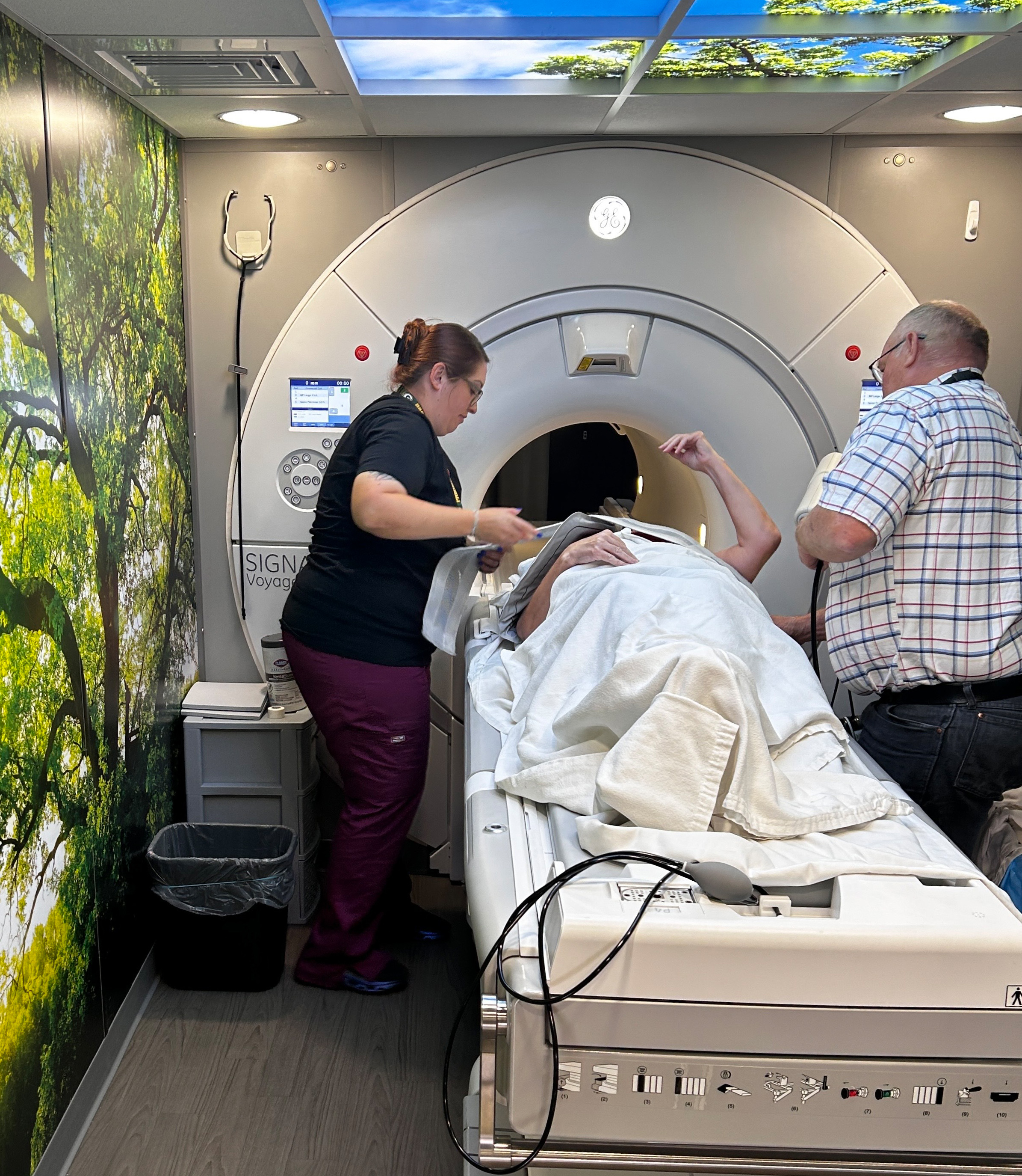 A person attended to by a nurse and another man, lays down in front of an MRI machine
