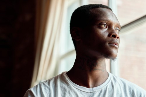 A man in a white tshirt stands in front of a window looking outwards
