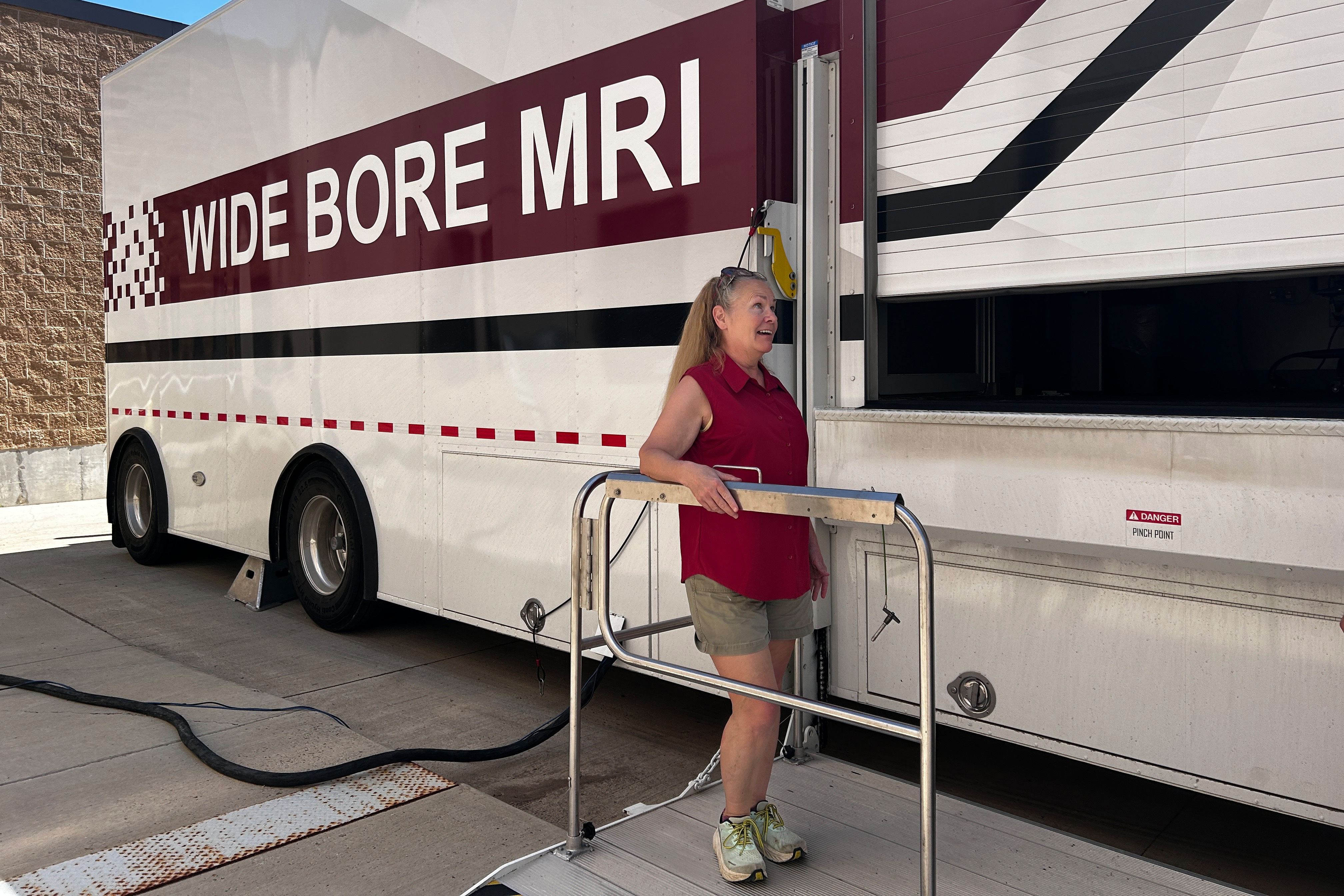 A photo of a woman posing in front of a mobile MRI unit.