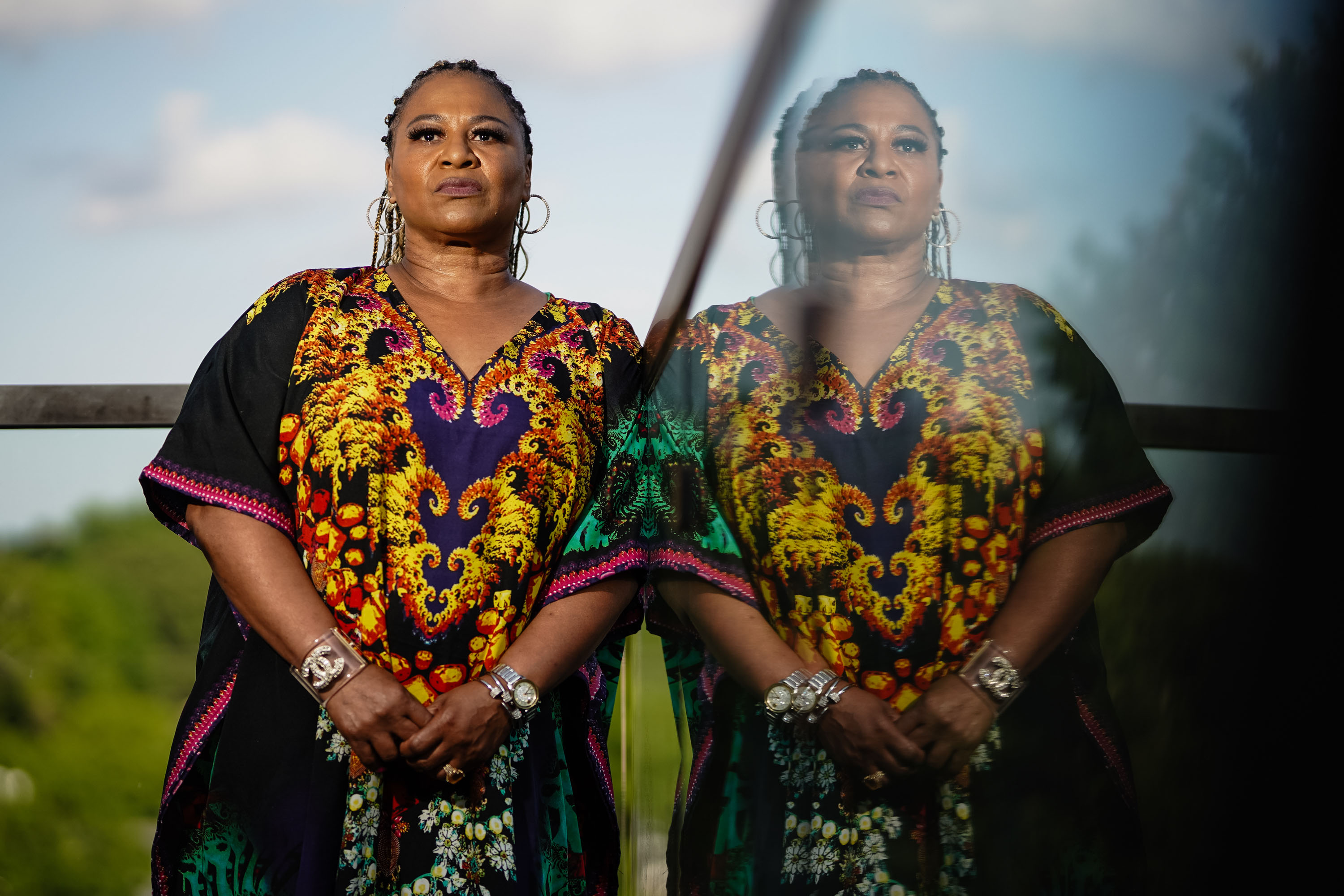 A portrait of a woman leaning against a glass balcony. Her semi-transparent reflection is visible in the right half of the image.