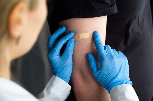 A photo of gloved hands putting a bandage on a patient's arm after giving them a vaccine.