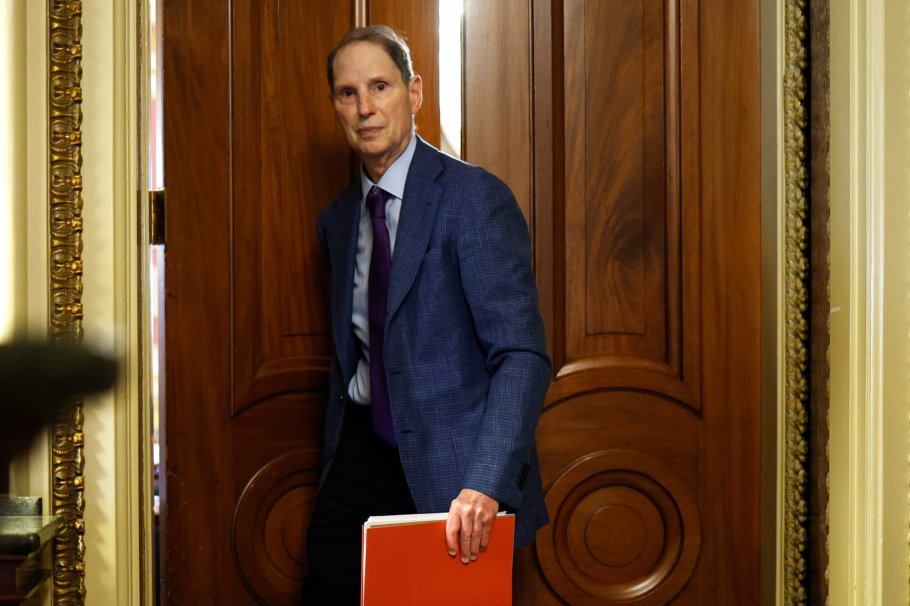 A photo of Sen. Ron Wyden, a file folder in hand, walking out of a doorway.