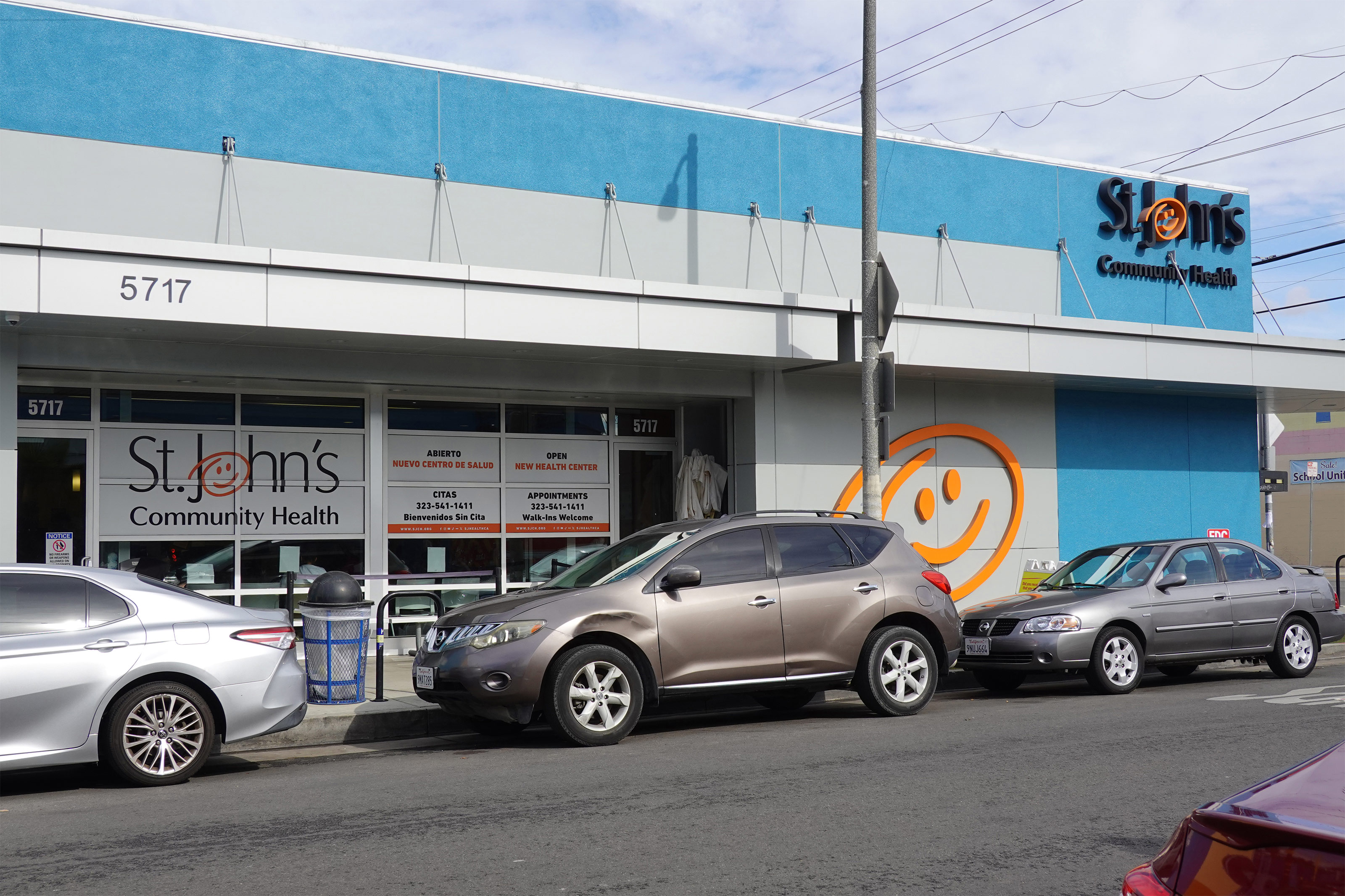 A photo of a health clinic's exterior. Cars are parked on the street in front of it.