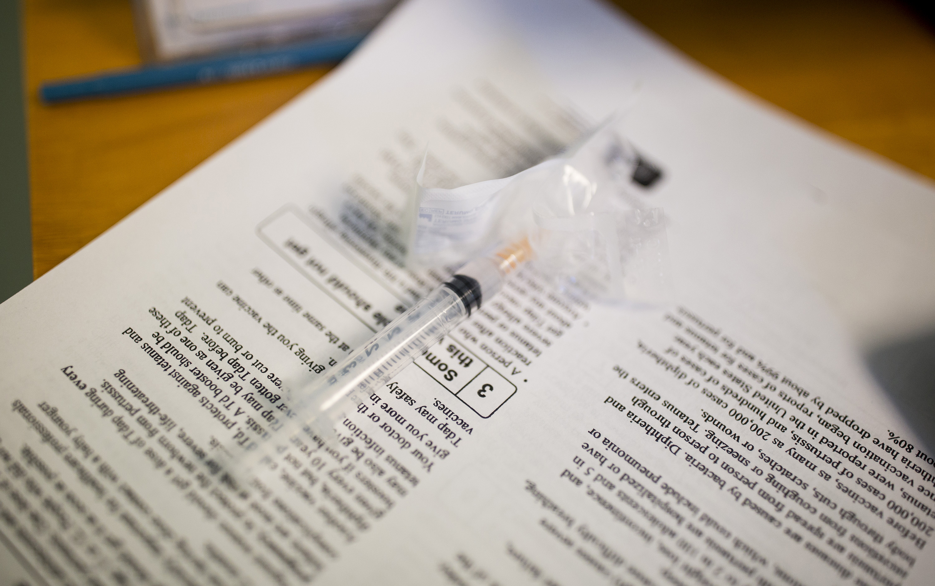 A syringe sits on top of paperwork on a desk