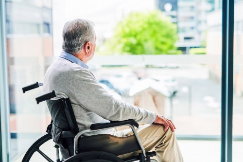 A photo of an older man looking out at a balcony in a wheelchair.