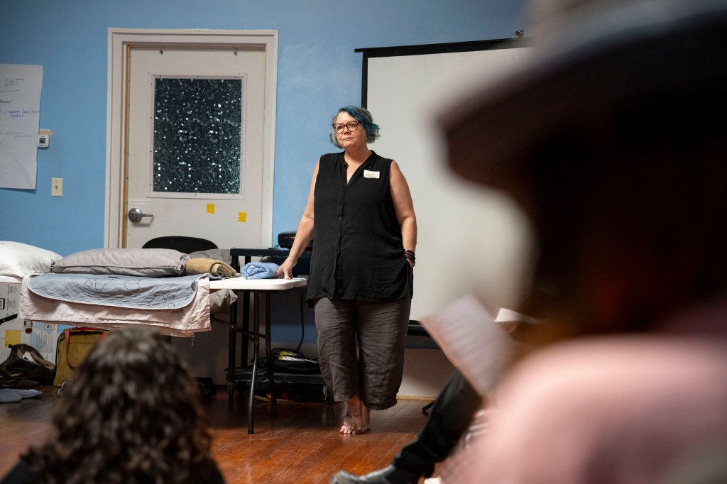 A woman stands in front of a group of people as she answers their questions.
