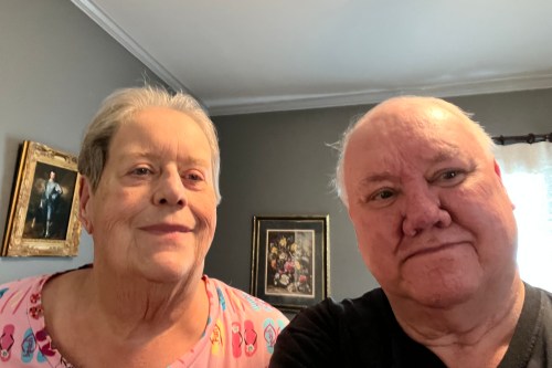 A senior man and woman seated in a room with several framed images behind them