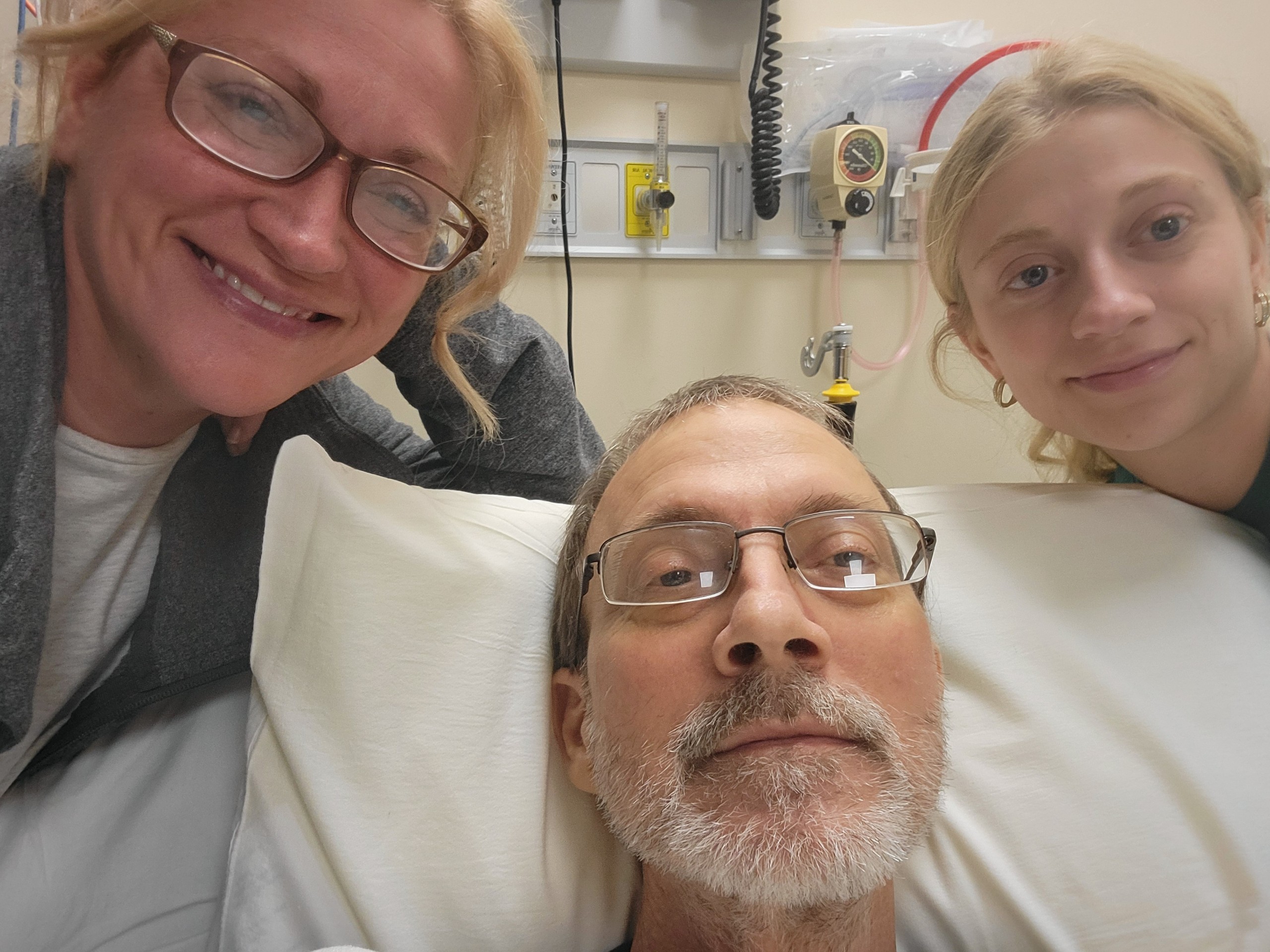 A photo of a man in a medical bed surrounded by his wife and daughter.