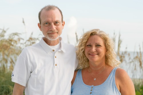 A photo of a husband and wife standing on the beach.