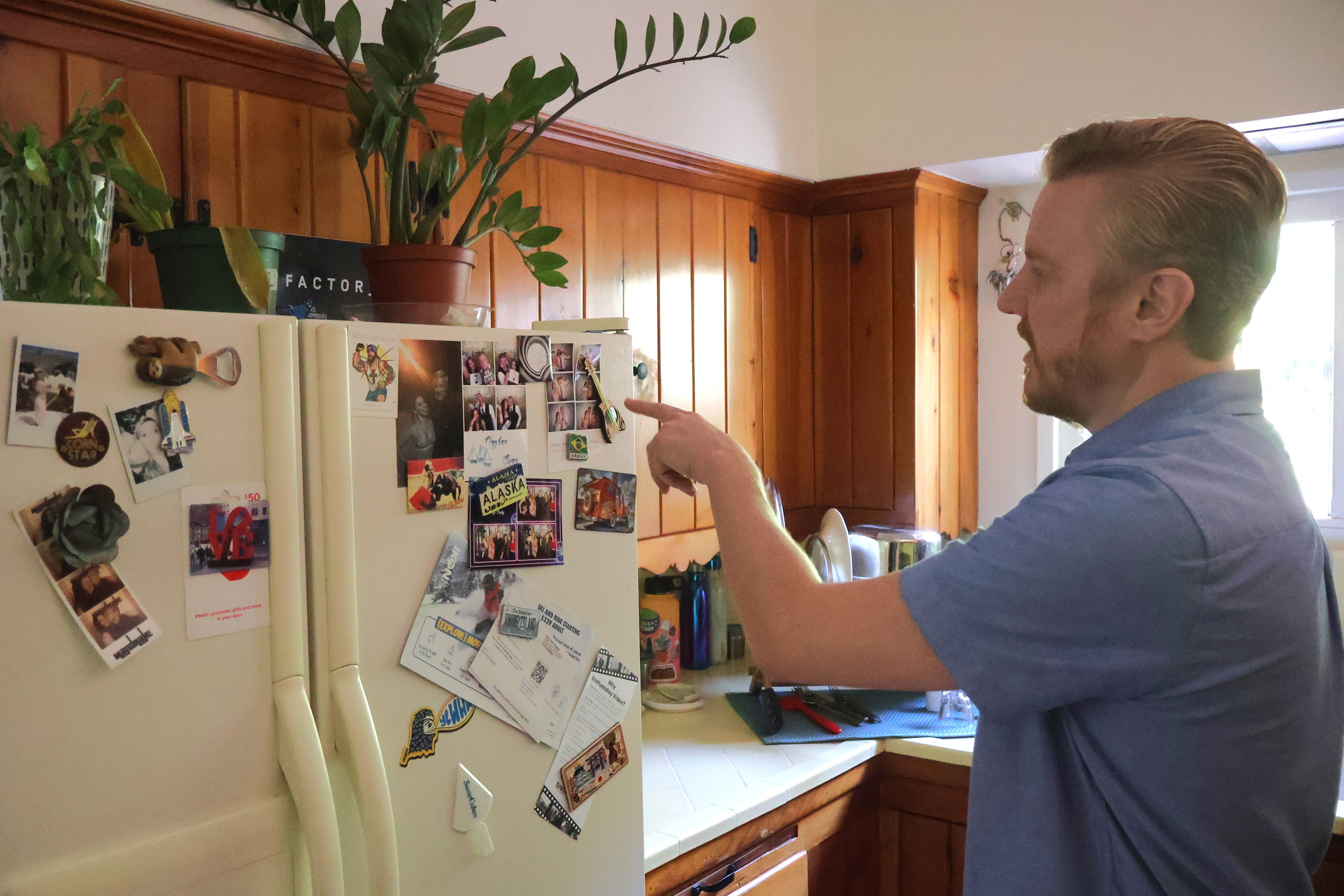 A photo of Kris Edwards pointing to photos on his fridge.