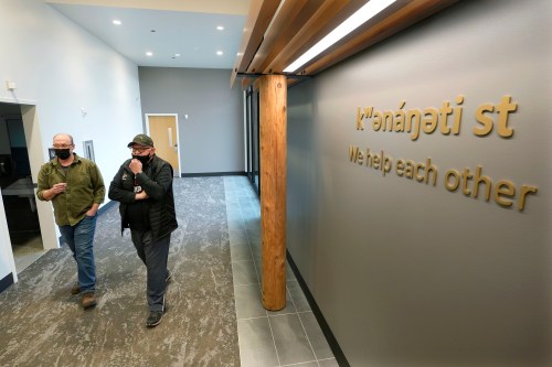 Two men walk beside each other in the hallway of a health clinic. Signage on the wall reads, "we help each other."
