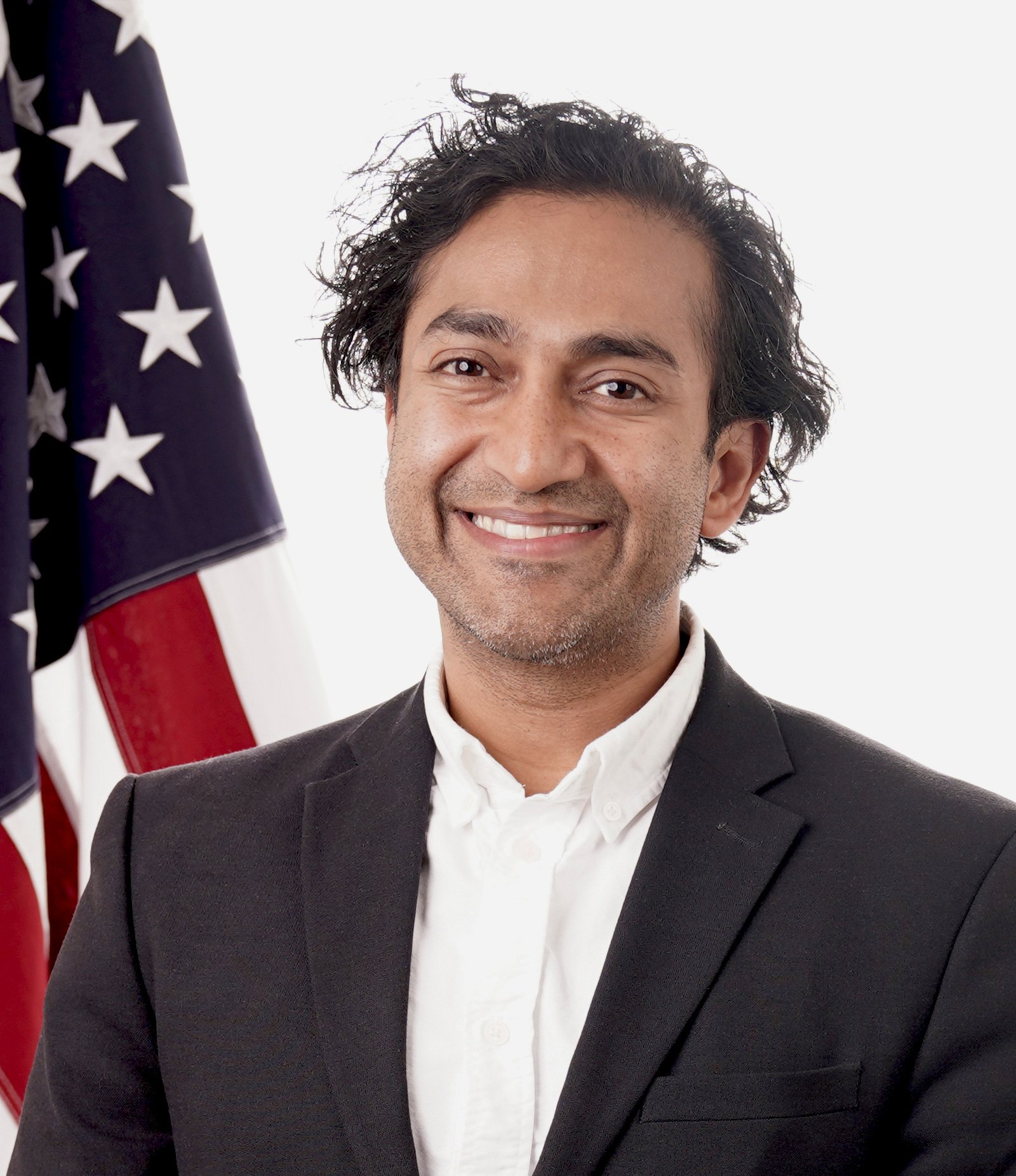 Vinay Prasad smiles for his official portrait. The U.S. flag is behind him.